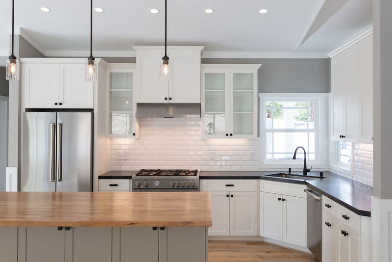 A bright, newly remodeled kitchen featuring white shaker cabinets, dark stone countertops, a stainless steel range, subway tile backsplash, and a butcher block island in the foreground.