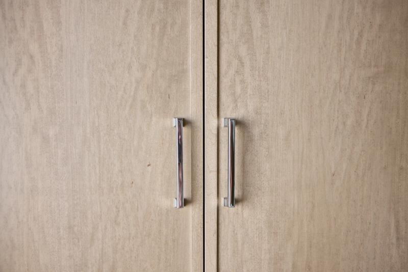 A close-up of two light wood cabinet doors with sleek vertical chrome bar pulls, showcasing a clean modern finish and natural wood grain texture.
