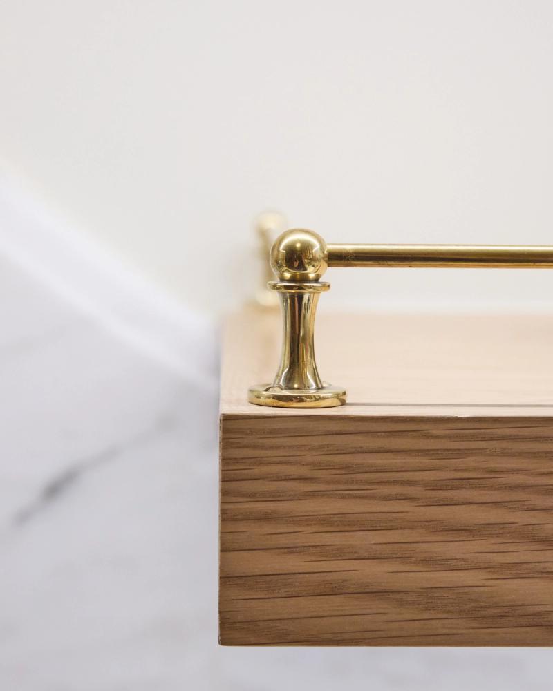 A close-up detail shot of a floating walnut wood bathroom vanity featuring a polished brass towel bar with a decorative ball-top post, set against a white marble background.