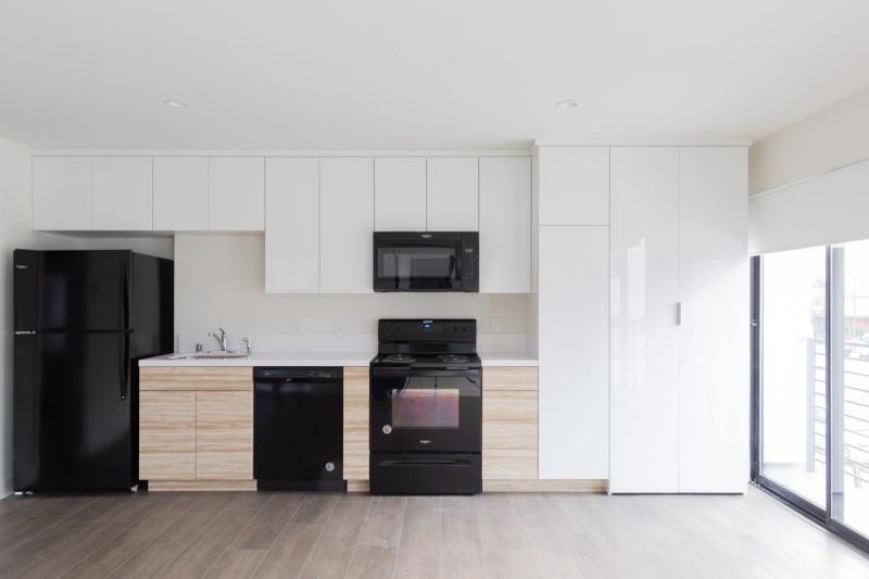 A modern kitchen featuring white high-gloss upper cabinets, light wood lower cabinets, black Whirlpool appliances including a refrigerator, range, dishwasher, and over-the-range microwave, with a sliding glass door to the right.