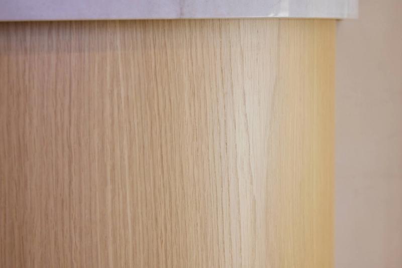 A close-up detail shot of a curved white oak wood panel base on a bathroom vanity or cabinet, topped with a light stone or marble countertop edge.