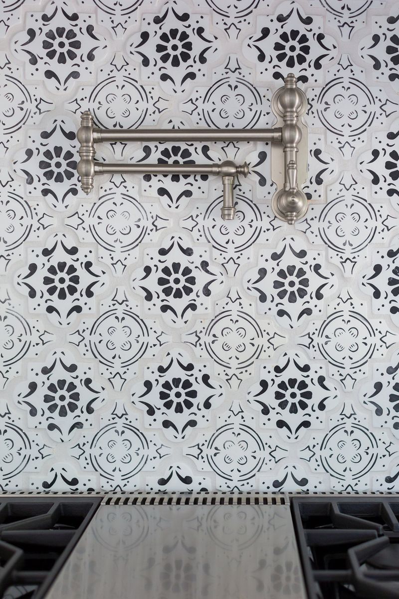 A detailed view of a black and white patterned tile backsplash behind a gas range, featuring an articulating brushed nickel pot filler faucet mounted to the wall.