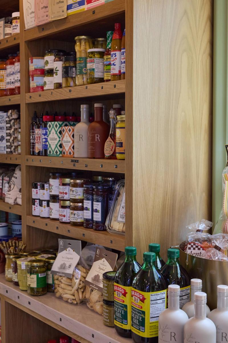 A custom oak built-in shelving unit stocked with gourmet pantry goods including olive oils, jams, sauces, and specialty foods in a retail or kitchen setting.
