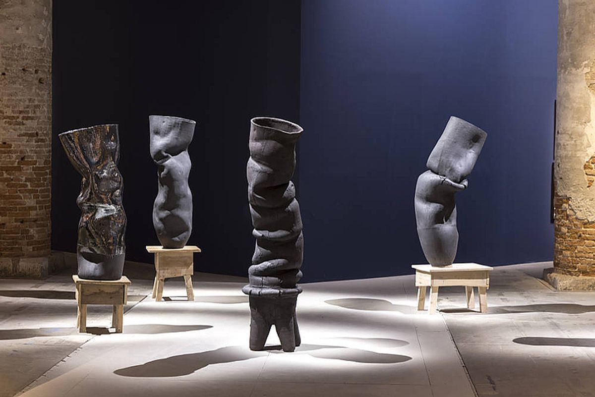 Ring of black stoneware vessels on wooden stools in the Arsenale.