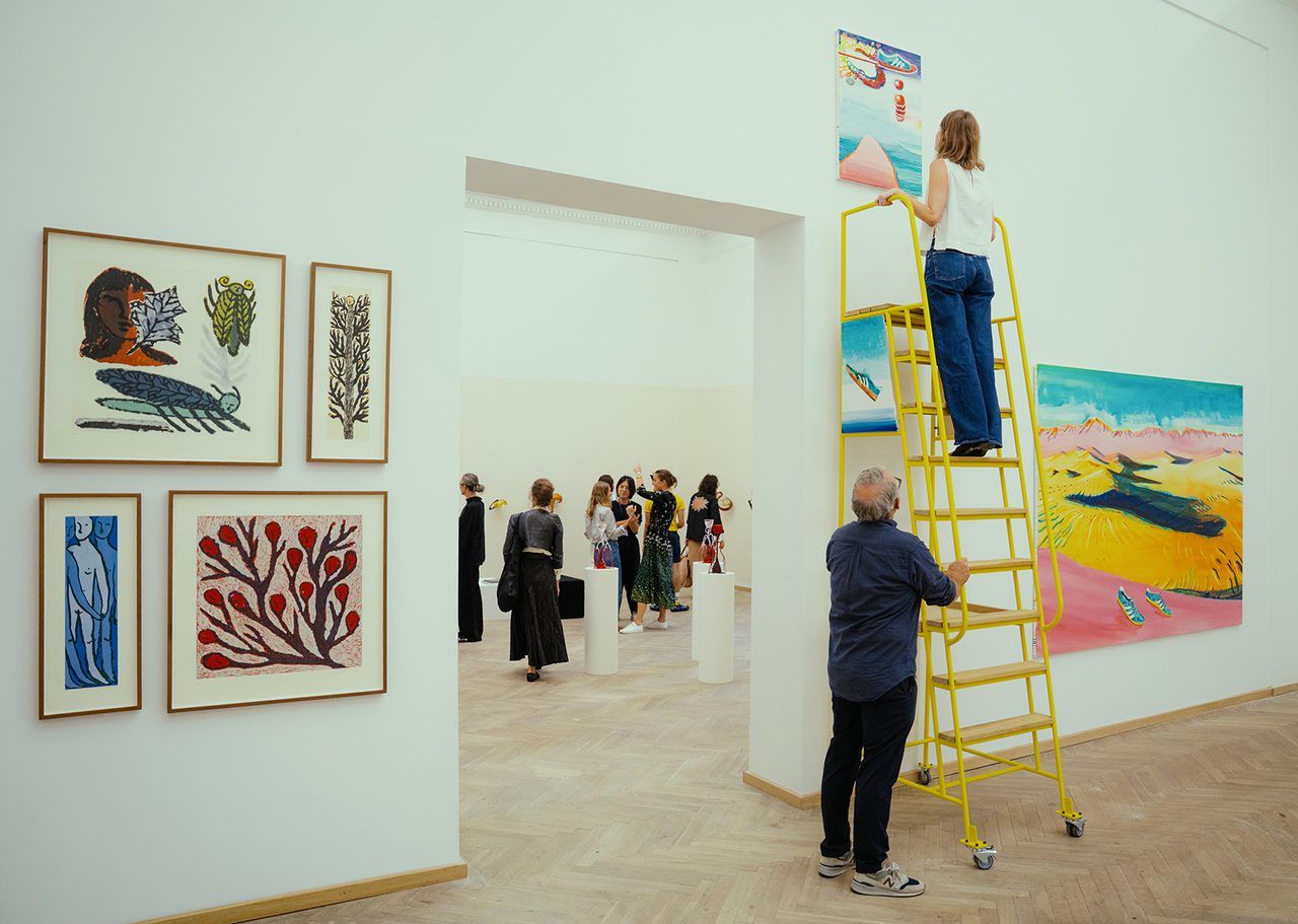 An installer on a yellow ladder hangs a painting in a gallery at Kunsthal Charlottenborg.