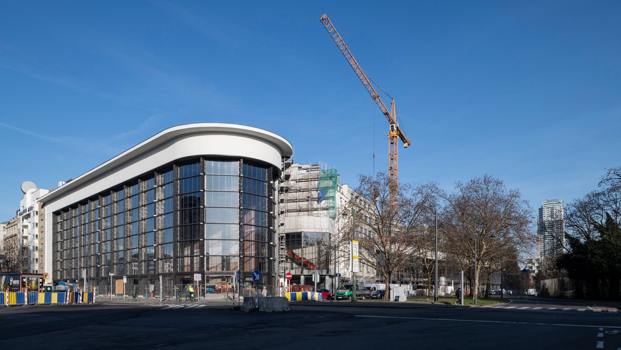 The curved glass facade of the former Citroën garage housing KANAL-Centre Pompidou, a construction crane still standing behind it.