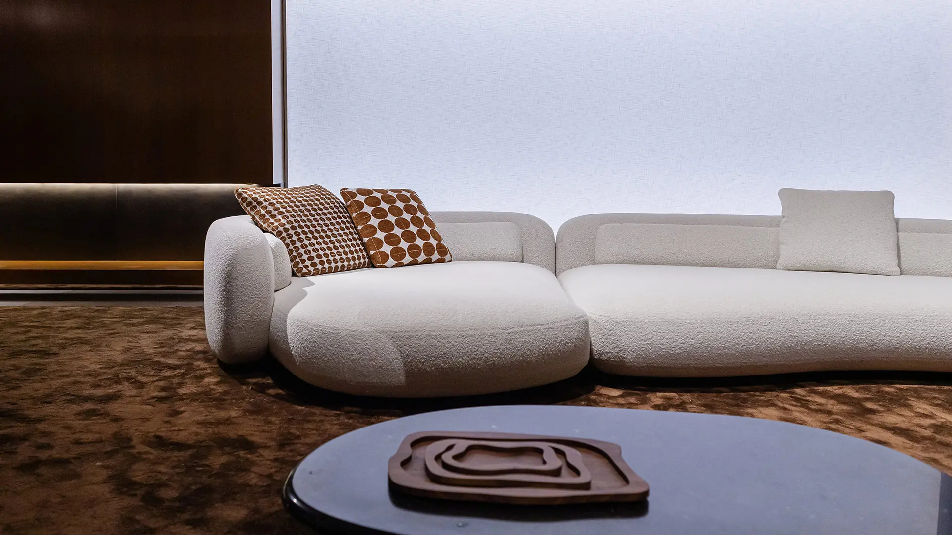 A curved white bouclé sofa with patterned cushions at Salone del Mobile.Milano 2026.