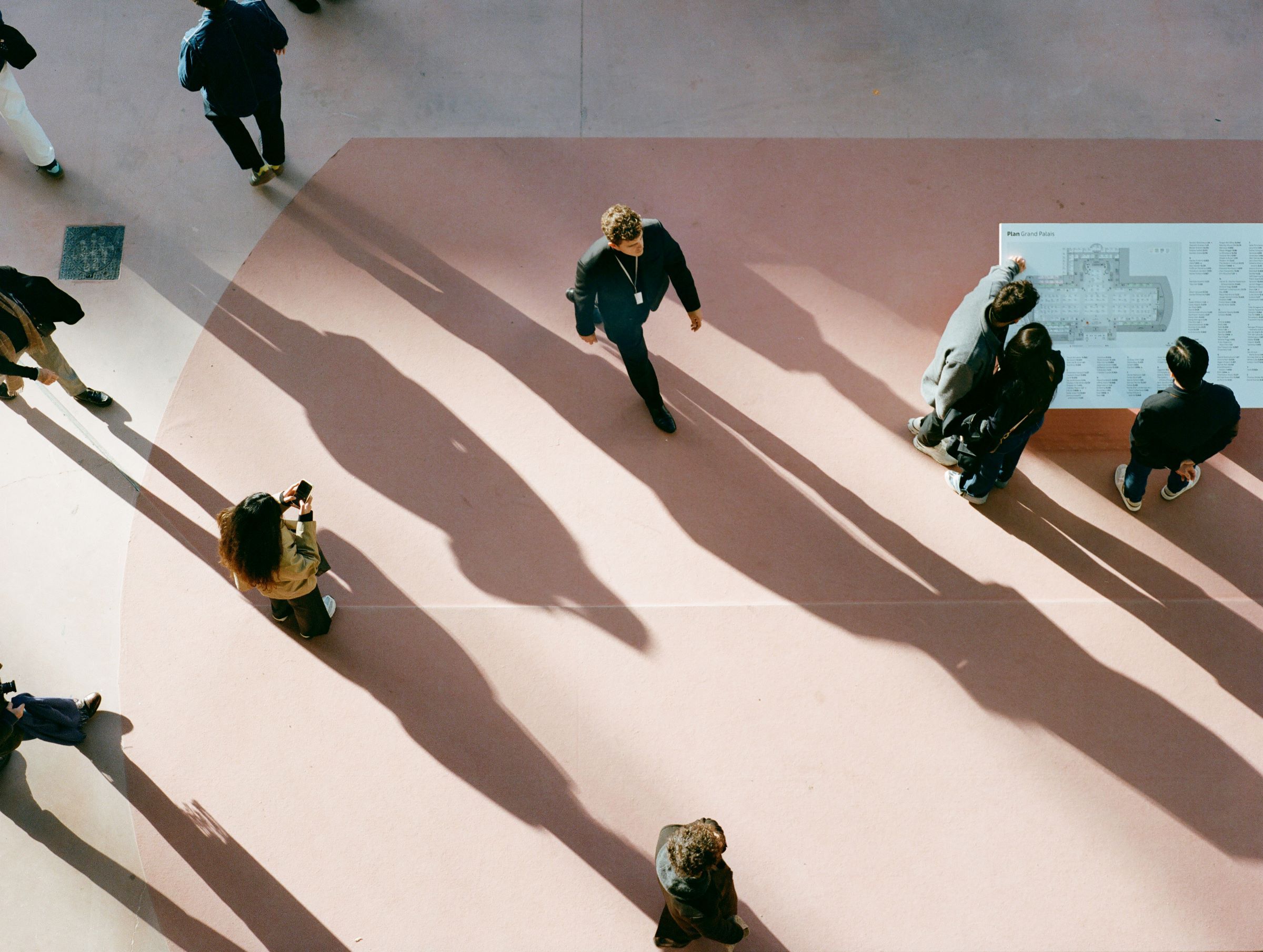 Overhead view of visitors and long shadows on the pink fair floor of the Grand Palais during Art Basel Paris.