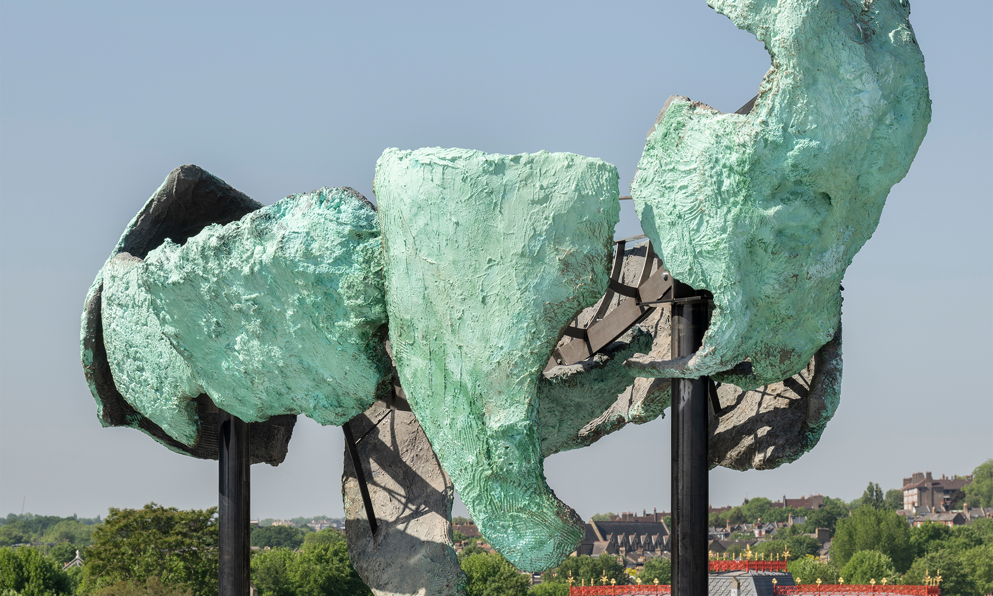 Emii Alrai's Guardian, a fragmented sculpture in weathered blue-green patina held on dark steel posts against open sky.