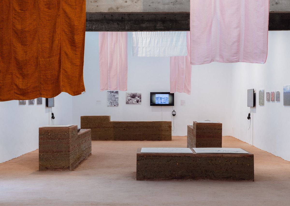 Gallery view inside the Brazilian Pavilion 'Terra' with earth floor and wall displays on indigenous and Quilombola territories.