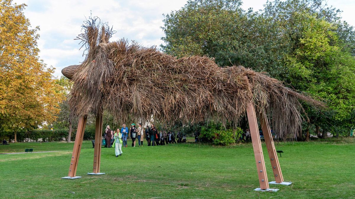 Assemble's Fibredog, a large shaggy dog-shaped shelter of thatch and salvaged timber, in the English Gardens at Frieze Sculpture 2025.