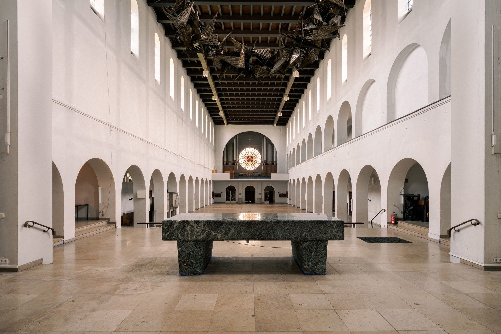 The white nave of Christ König church in Bochum with a cluster of dark metal stars suspended from the ceiling.