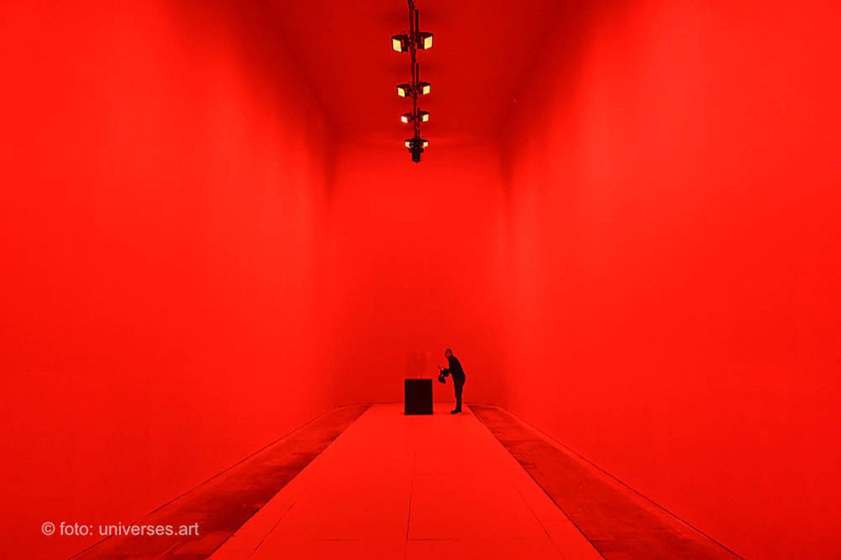 Small metal cube displayed alone under crimson light in a dark room.