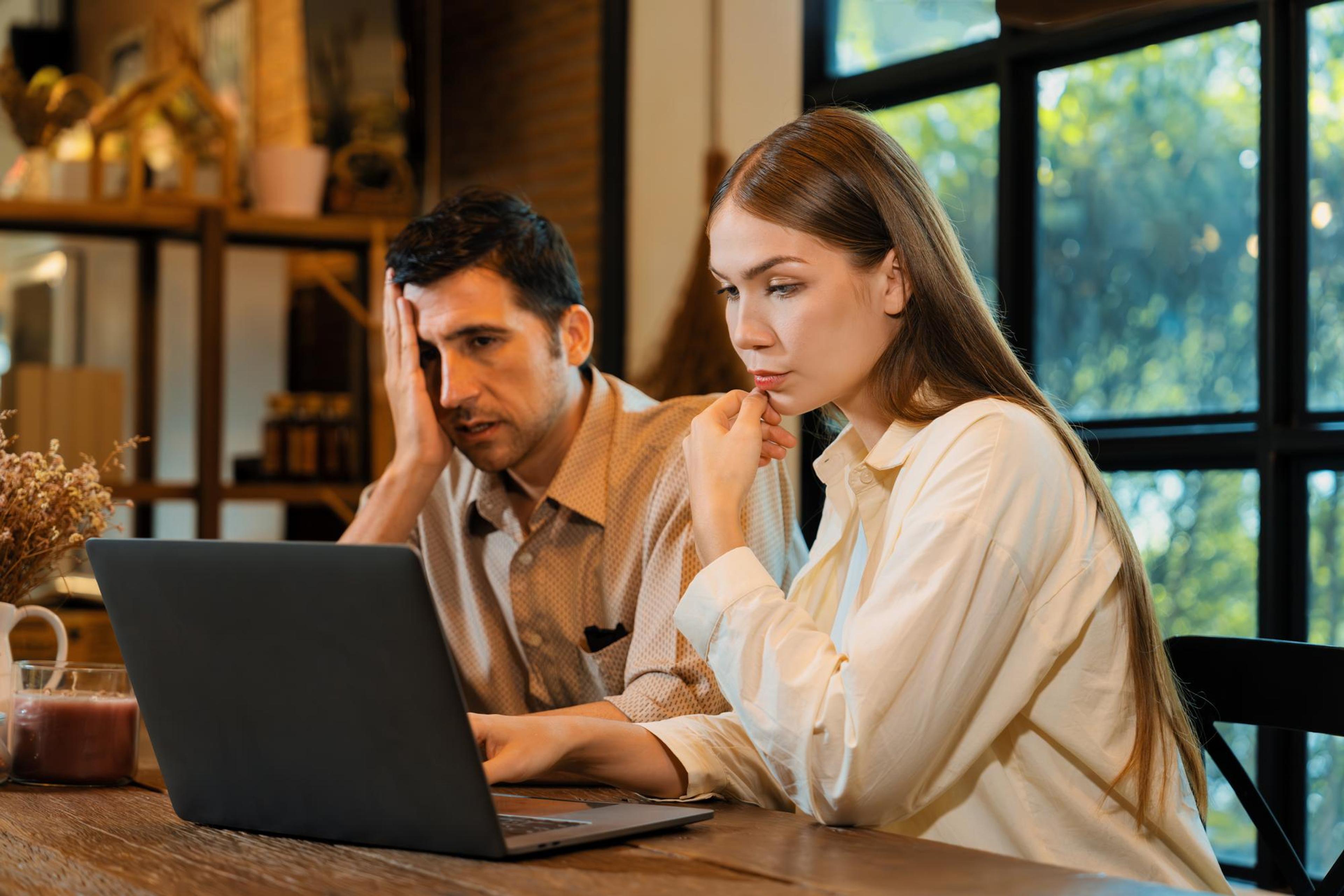 Мужчина и женщина с напряжённым видом смотрят на ноутбук в офисе с большими окнами.