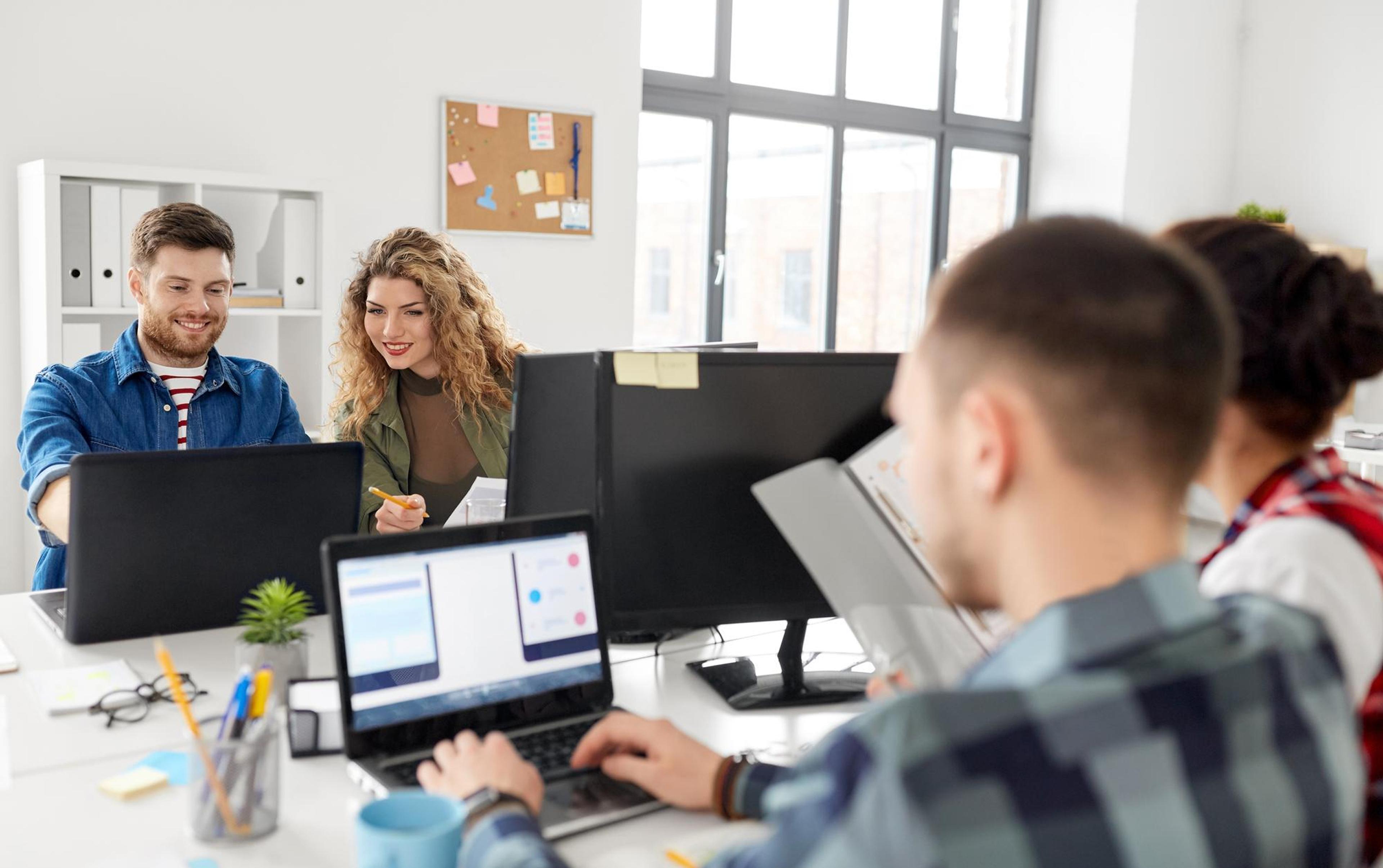 Group of colleagues collaborating at a desk with laptops in a modern office.