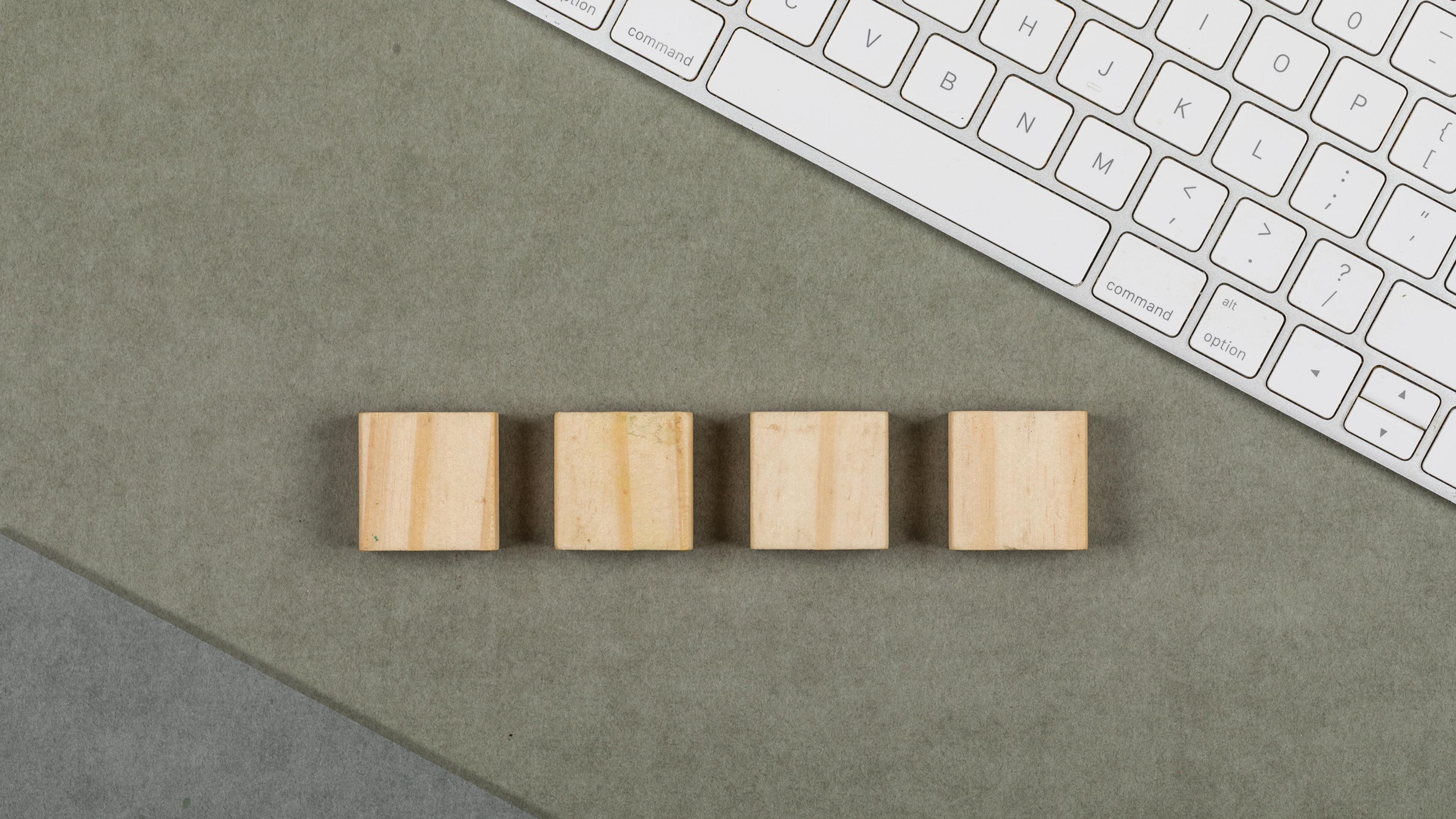Vier kleine Holzwürfel auf grauer Oberfläche neben einer weißen Tastatur