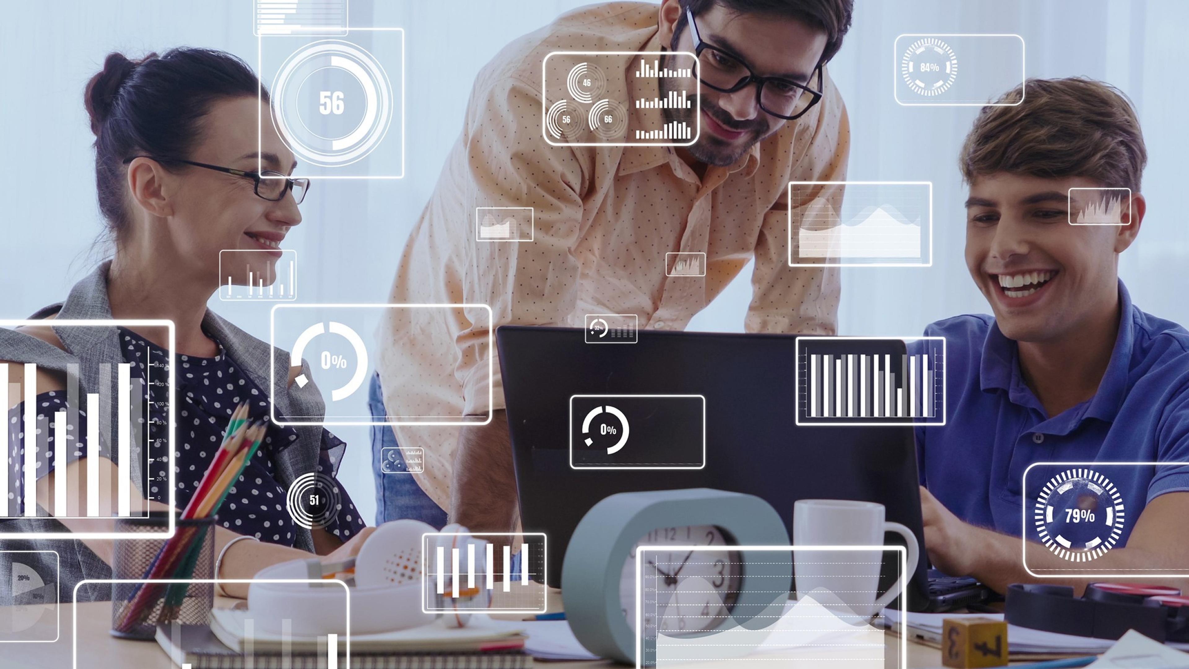 A group of people in an office with laptops and digital statistics on their screens