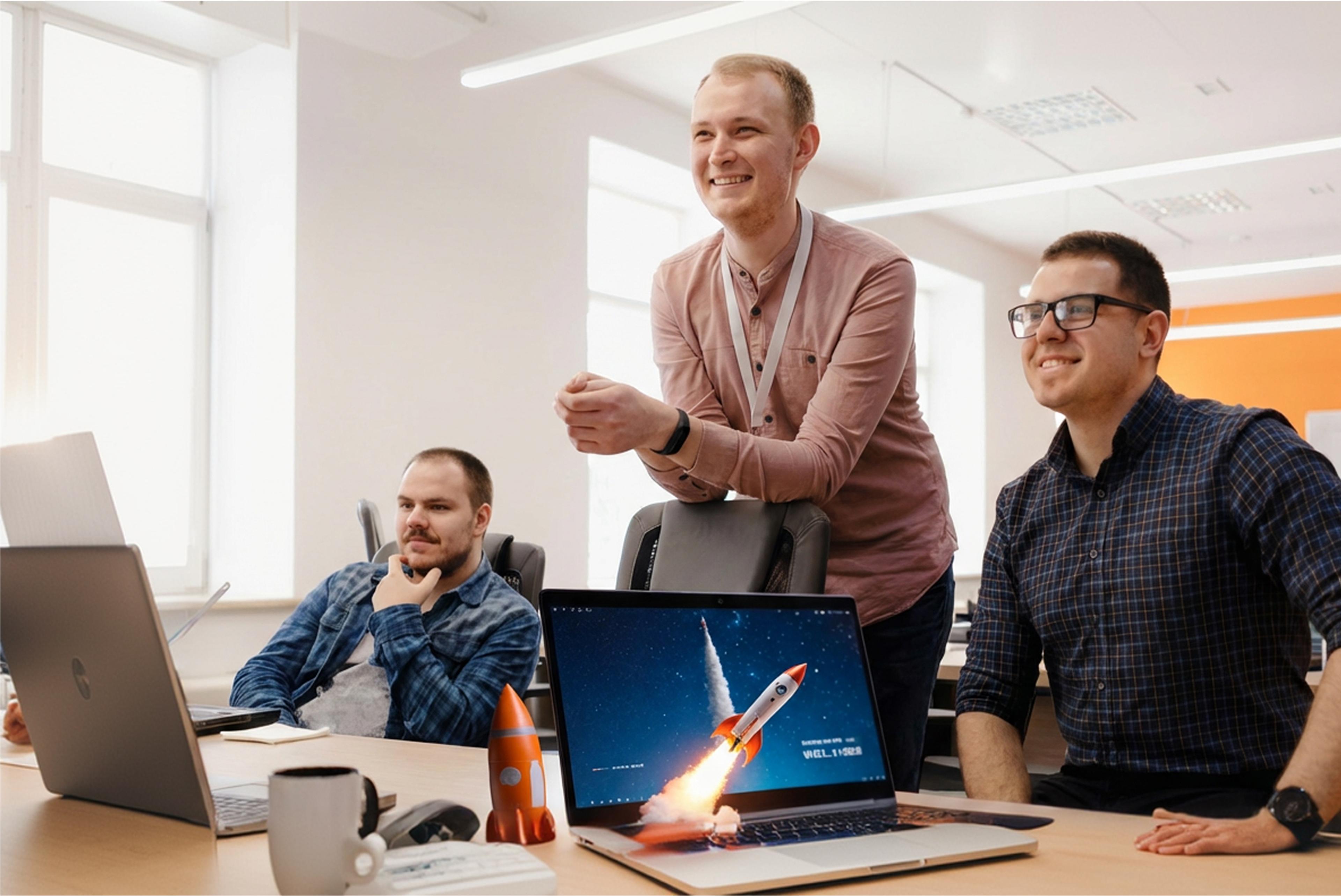 Drei Männer in einem Büro, diskutieren über Laptops. Raketenmodell auf dem Tisch.