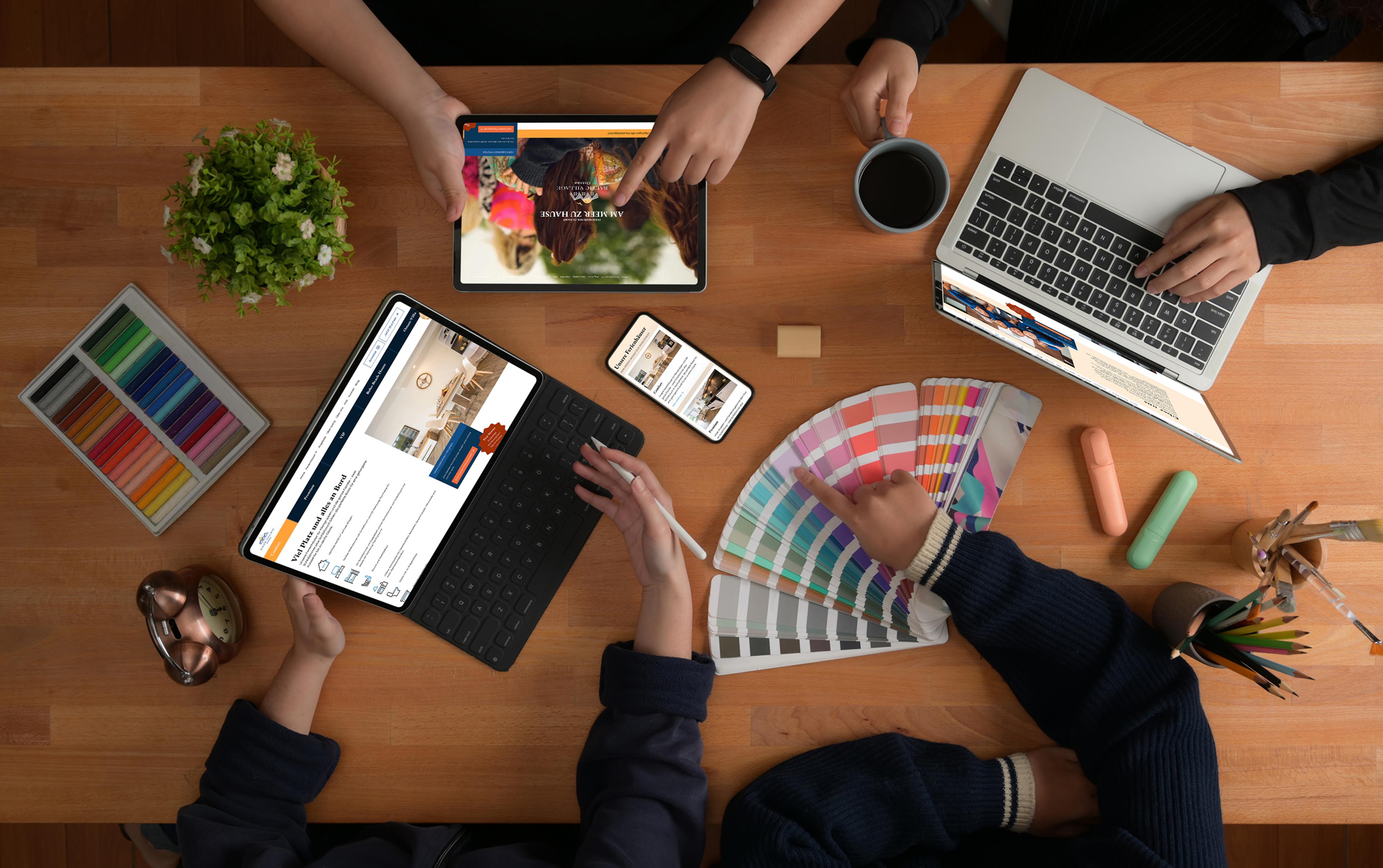 Moderne Arbeitsumgebung mit Laptop, Tablet, Smartphone und Farbabstimmungskarten auf einem Holztisch.