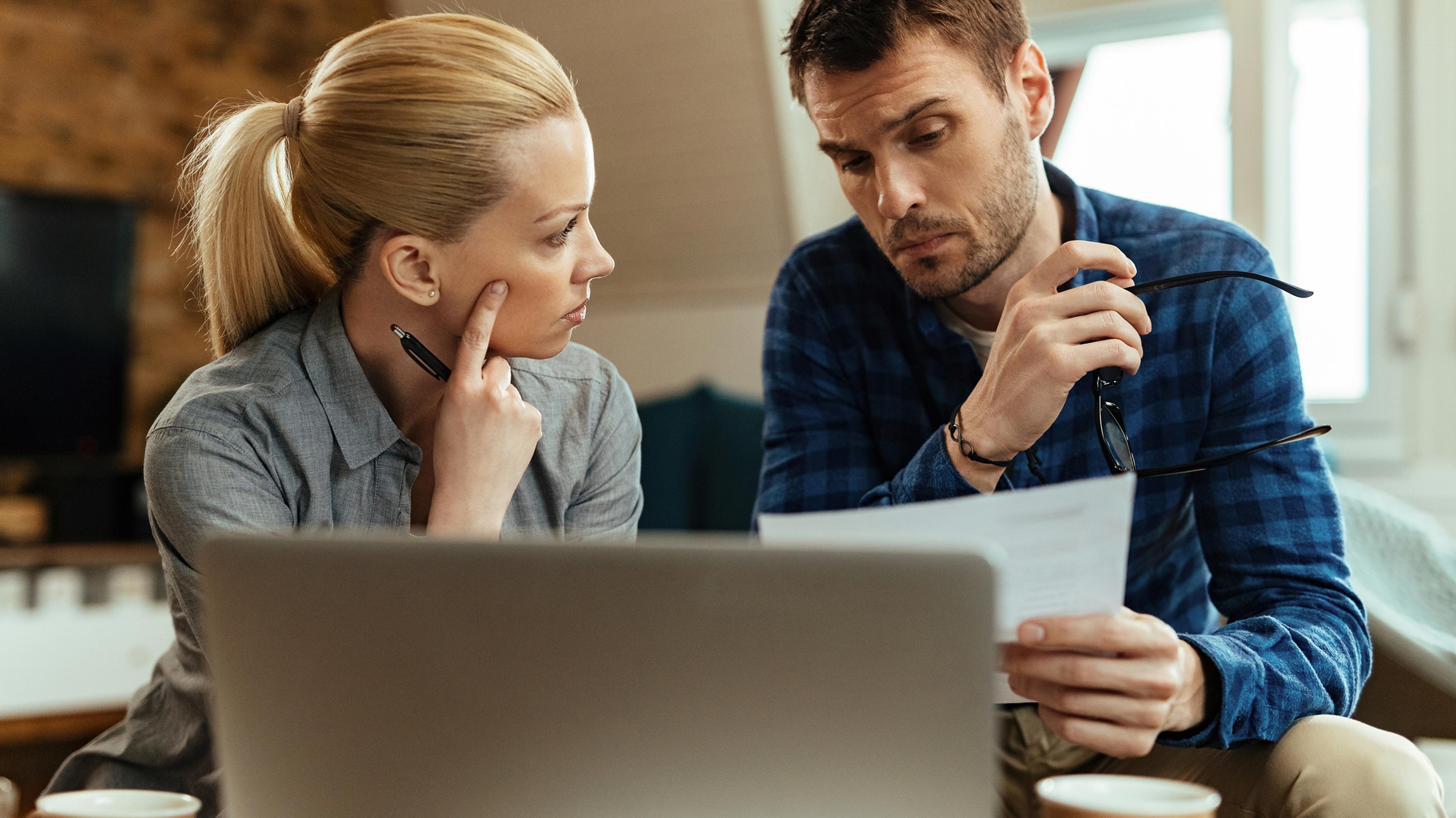 A woman and a man look together at a laptop with concentrated expressions