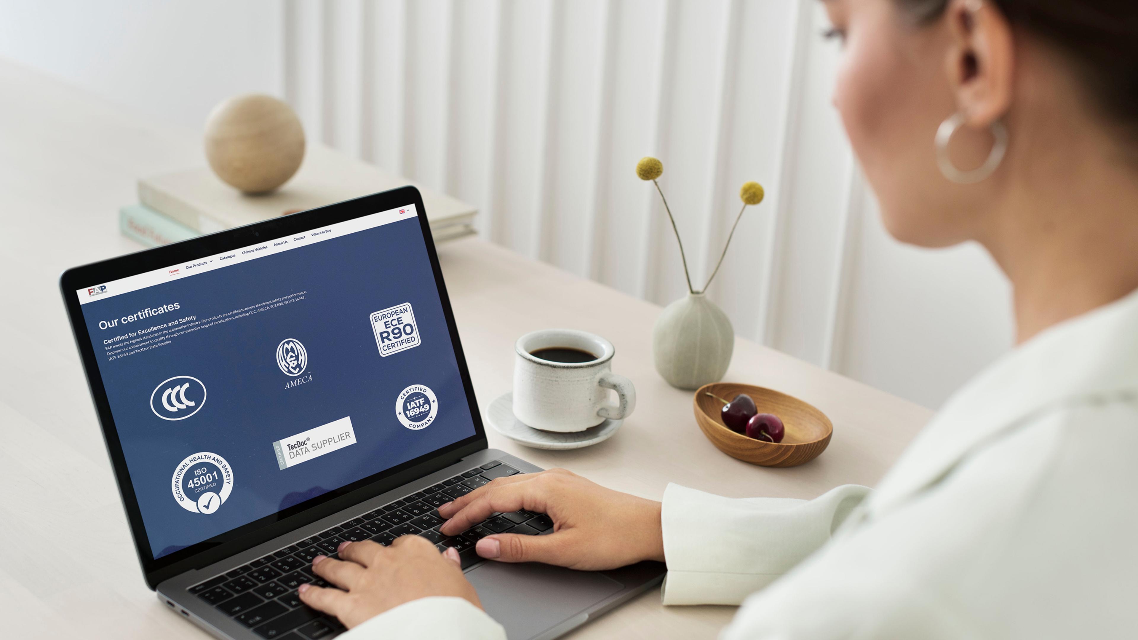 Frau am Schreibtisch mit Laptop, Kaffee und Kirschen; Zertifikate auf dem Bildschirm sichtbar