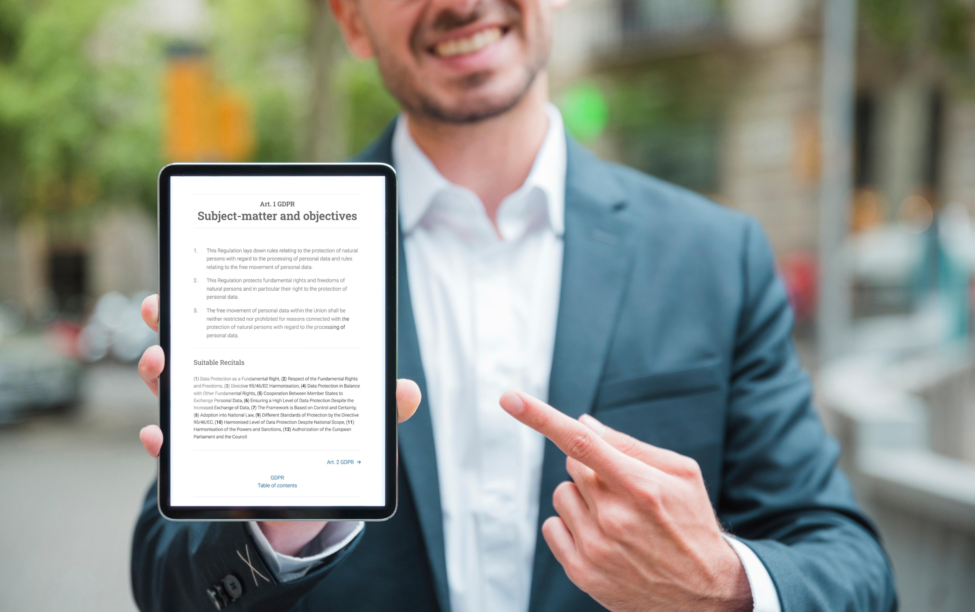Мужчина в костюме держит в руках планшет с регламентом GDPR и улыбается