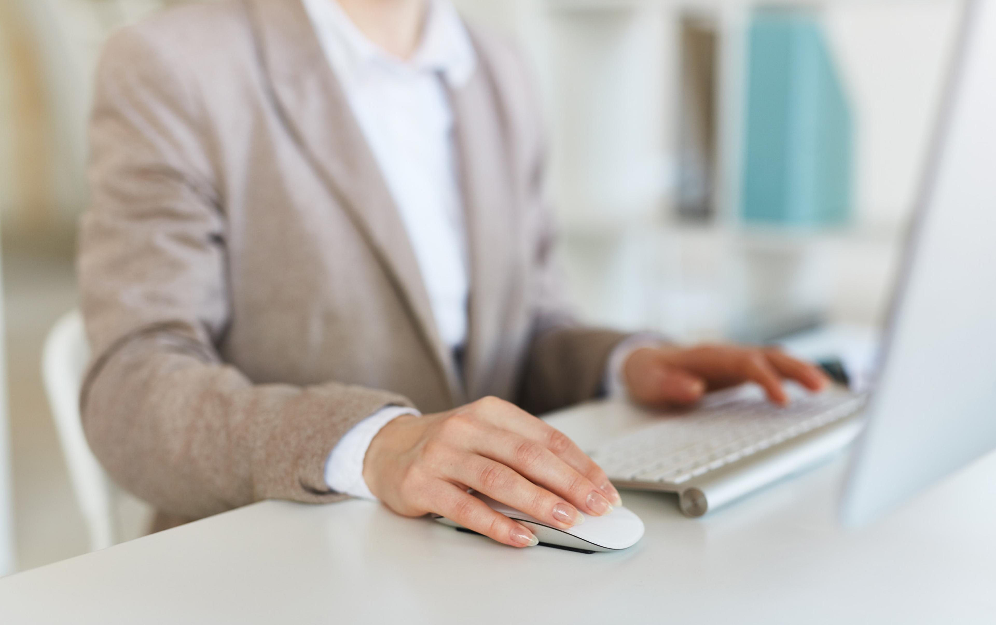 A woman in a beige blazer is using a computer mouse at her desk