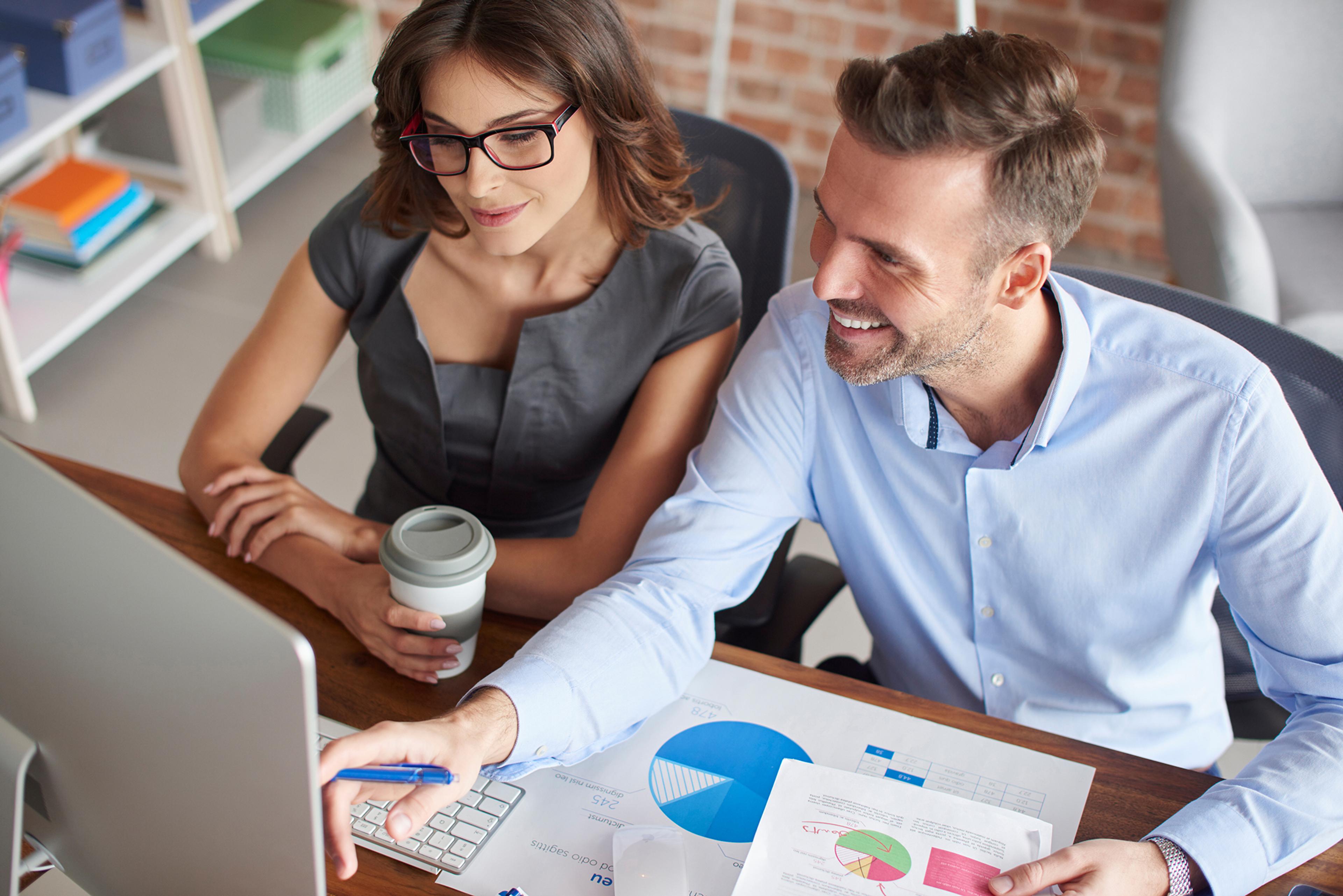 Двое коллег обсуждают деловые вопросы за компьютером в современном офисе.