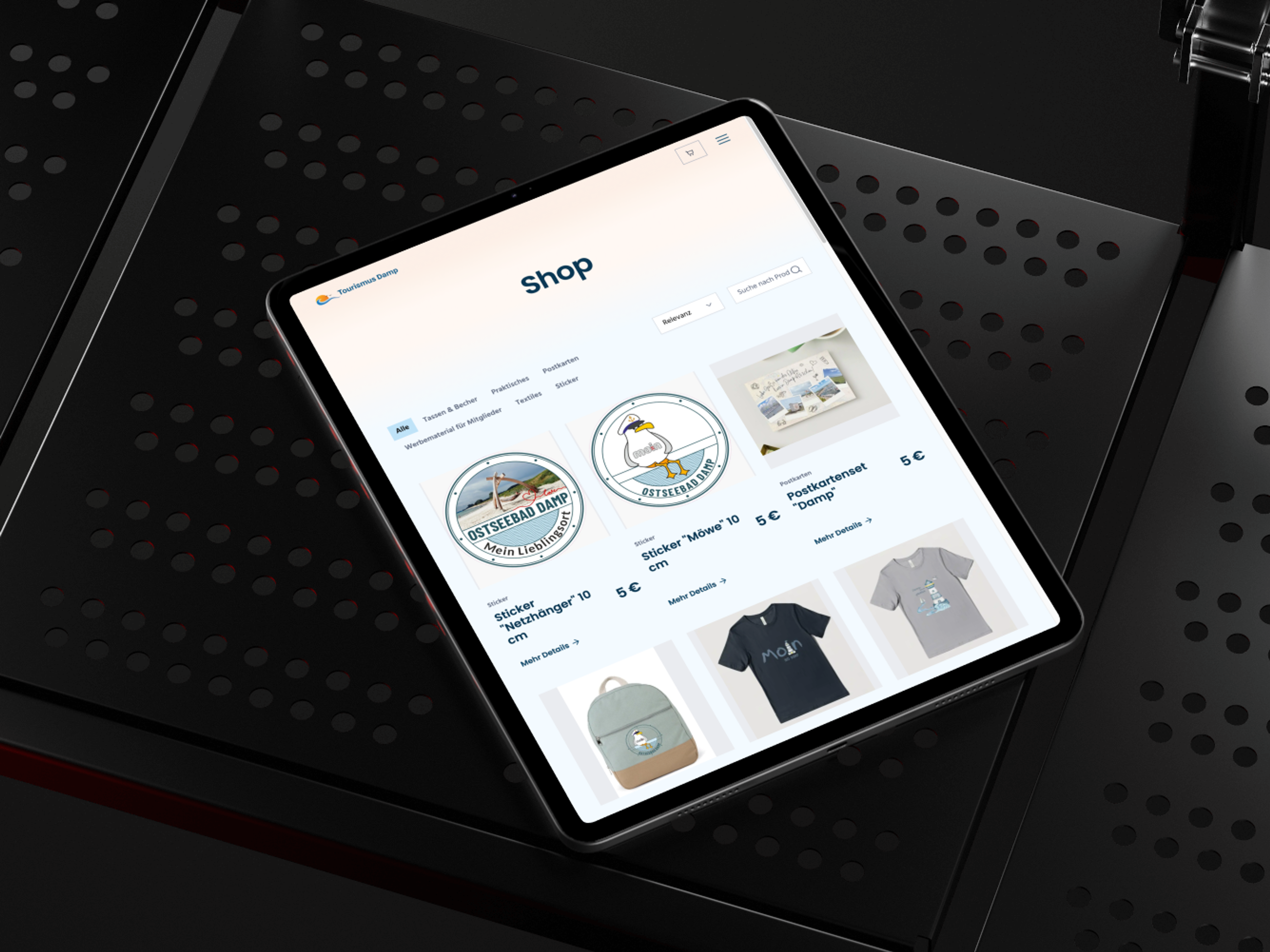 Ein Tablet zeigt eine Online-Shop-Seite mit verschiedenen Produkten wie Aufklebern und T-Shirts.