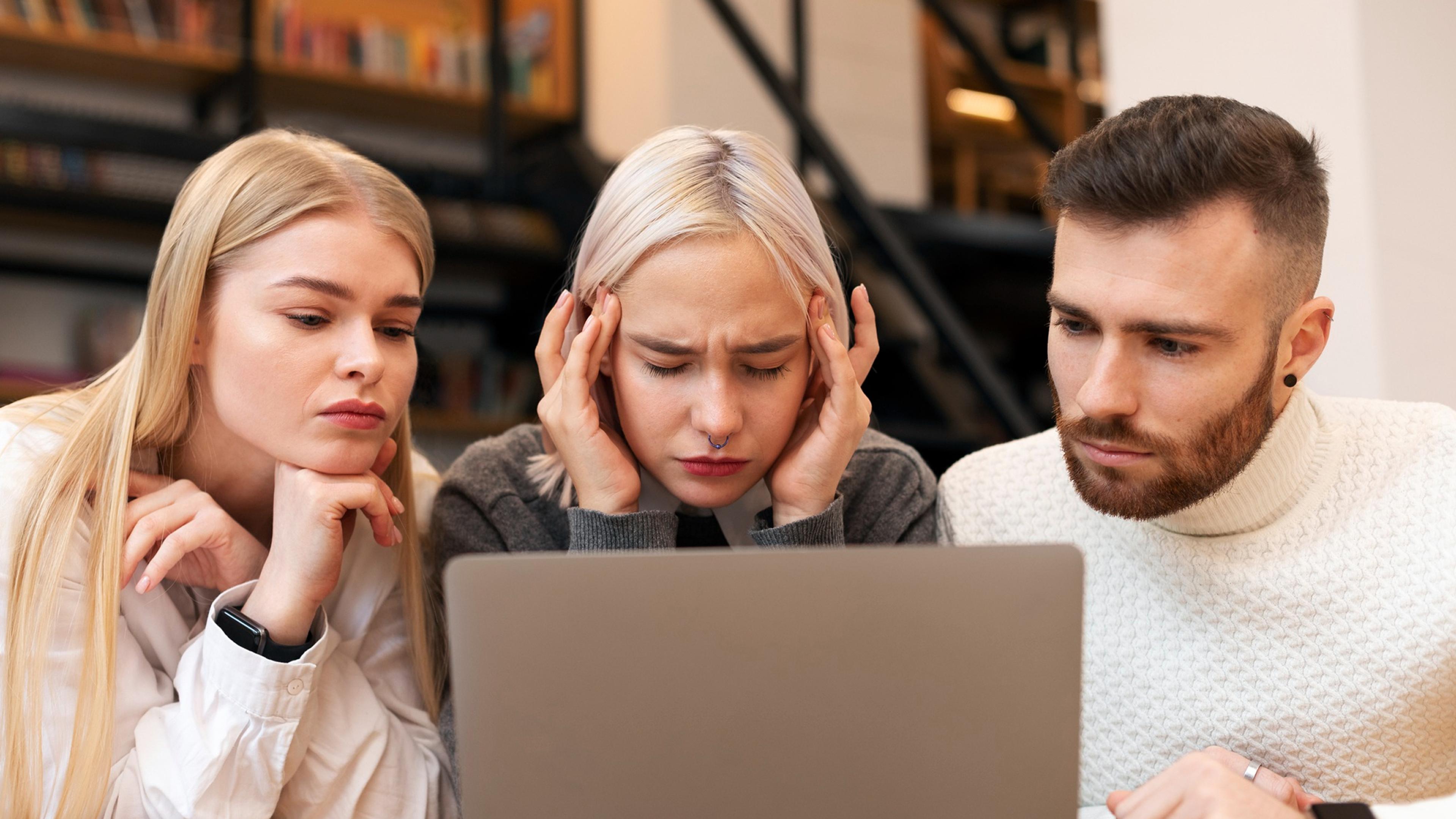 Zwei Frauen und ein Mann schauen mit ernsten Blicken konzentriert auf einen Laptop