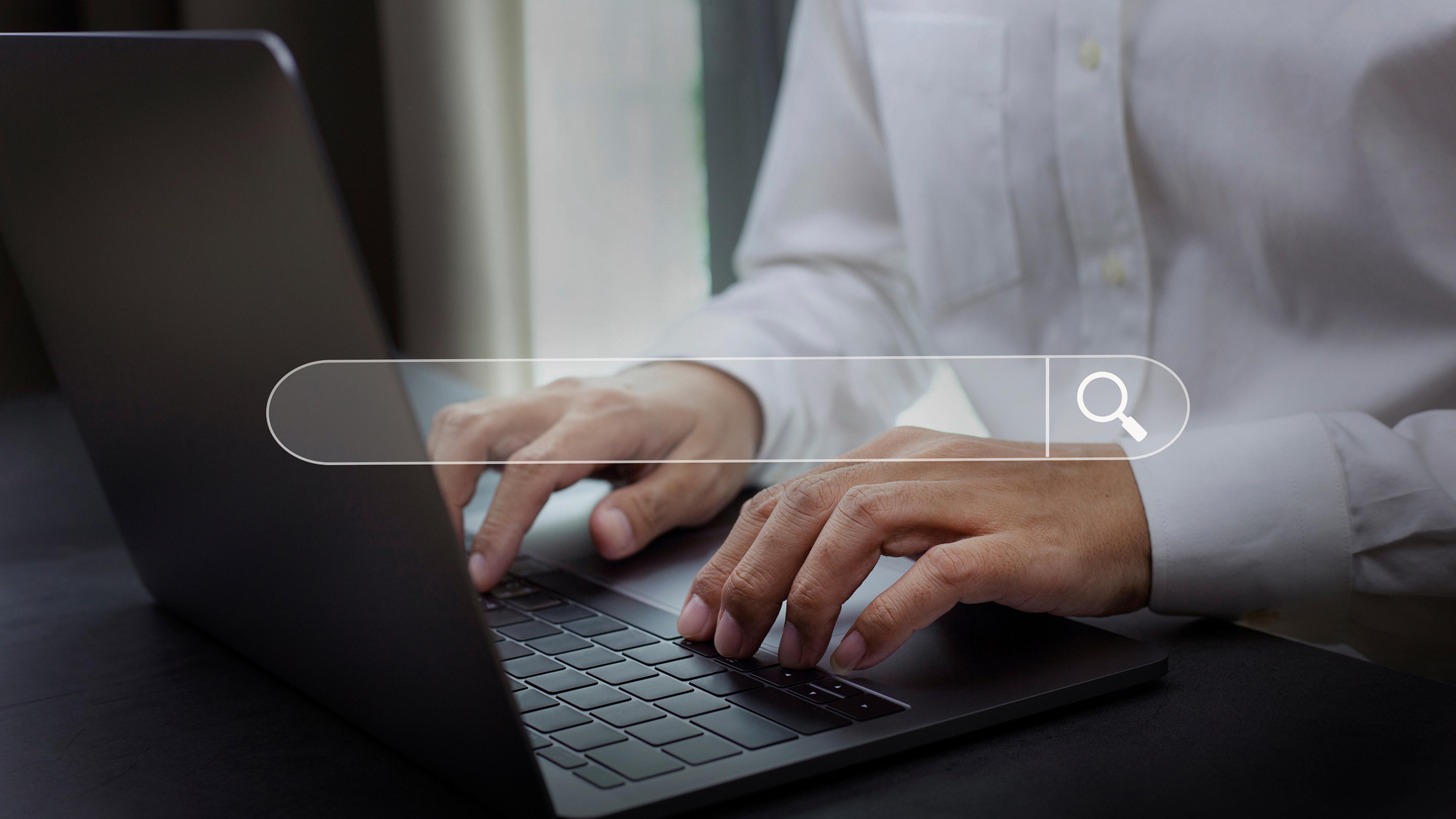 Hände einer Person tippen auf einem Laptop mit eingeblendeter Suchleiste