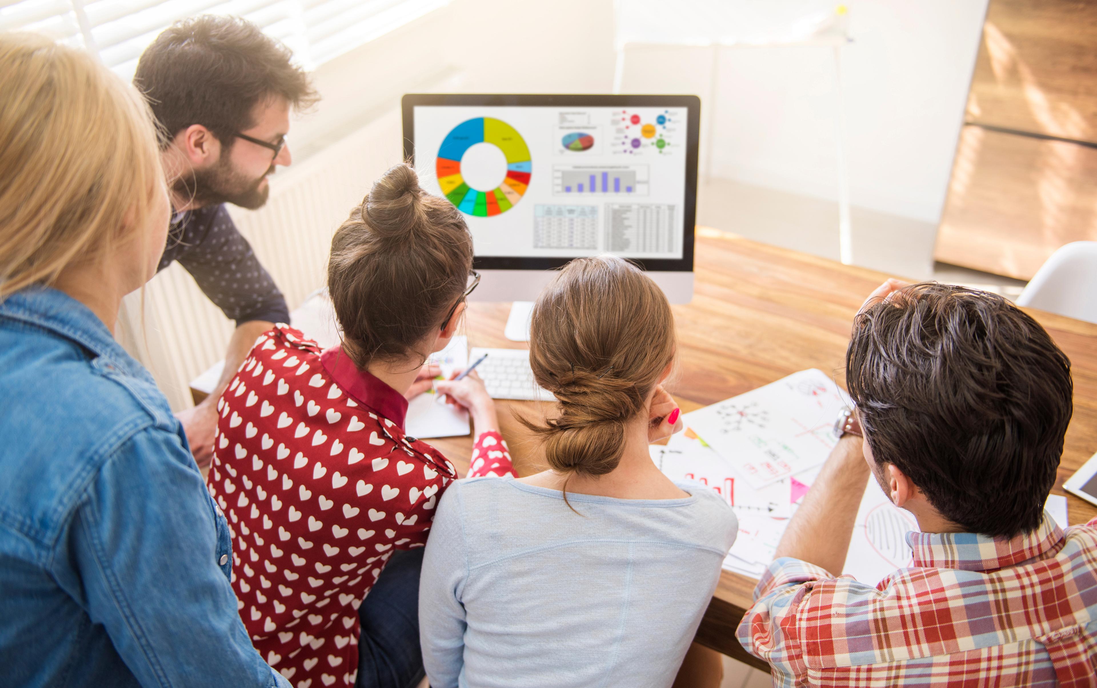 Menschen im Büro betrachten bunte Diagramme auf einem Computermonitor.