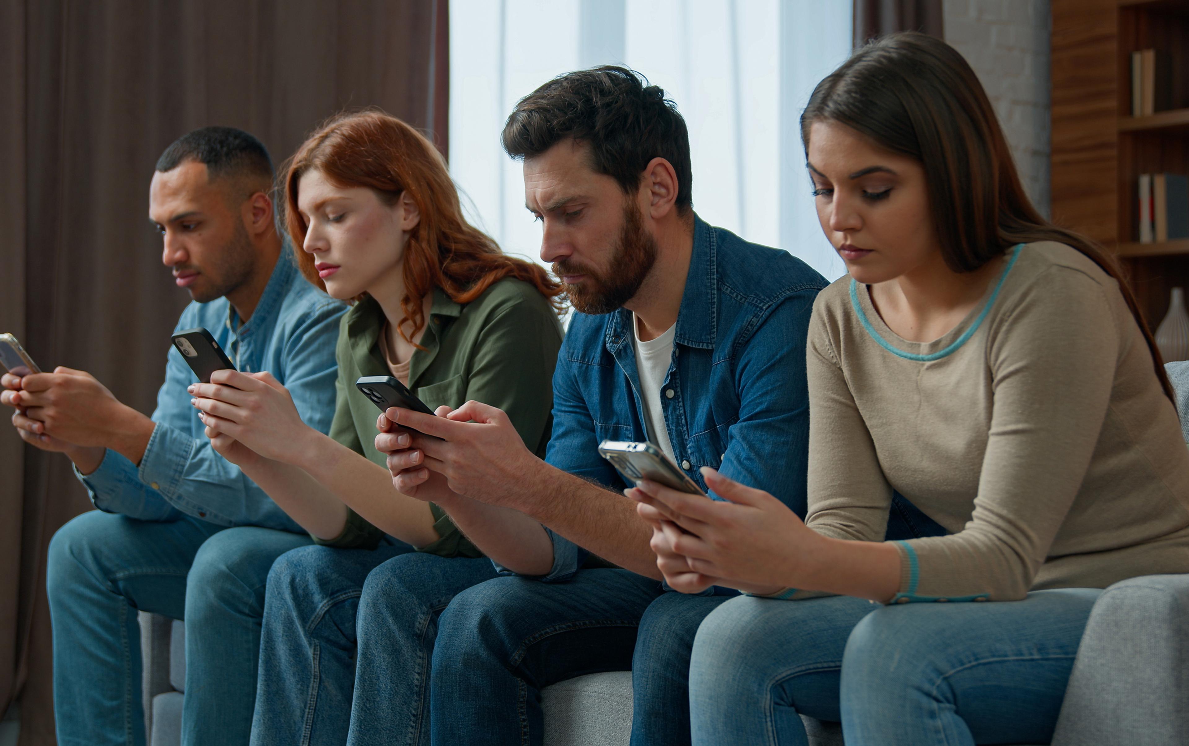 Vier Menschen in Freizeitkleidung sitzen nebeneinander auf einem Sofa und nutzen ihre Smartphones.