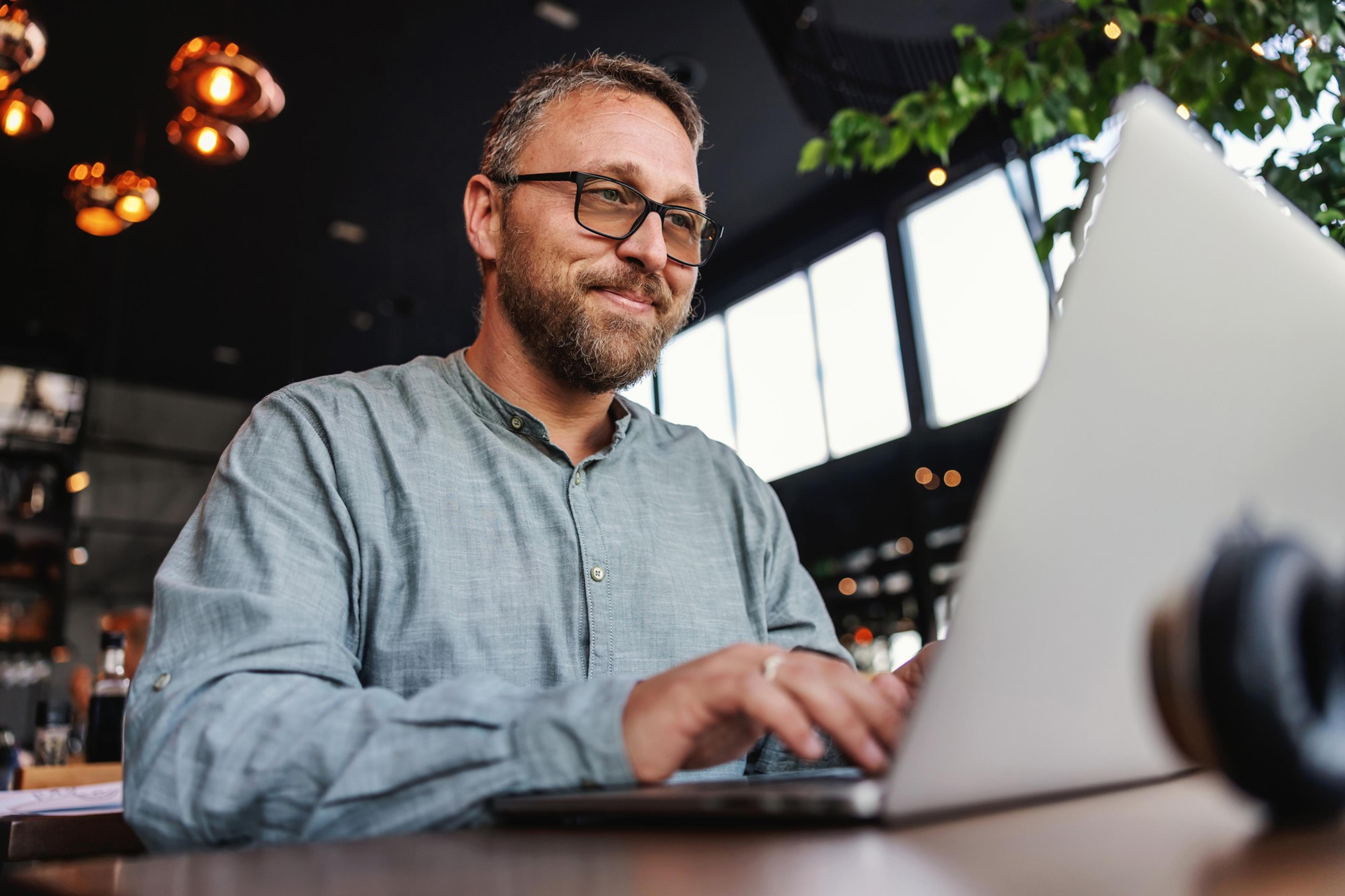 Mann mit Brille tippt auf einem Laptop in einem gemütlichen Café