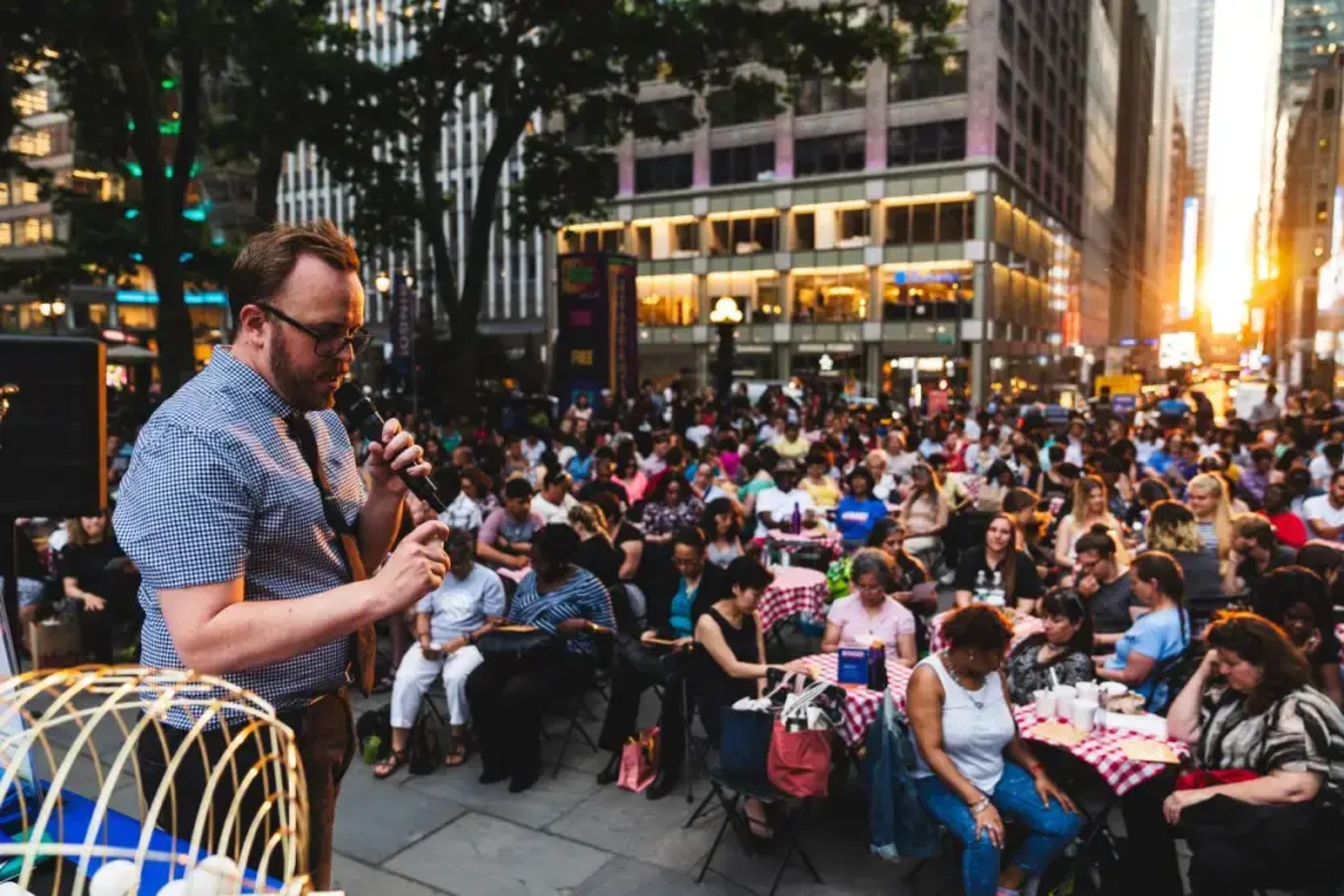 Man hosting Bingo in Bryant Park with guests sitting at tables