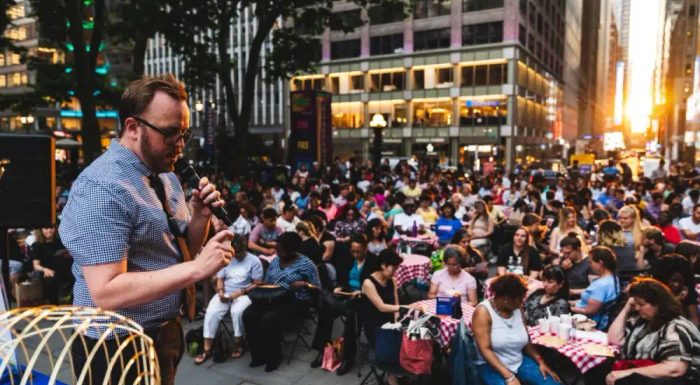 Man hosting Bingo in Bryant Park with guests sitting at tables