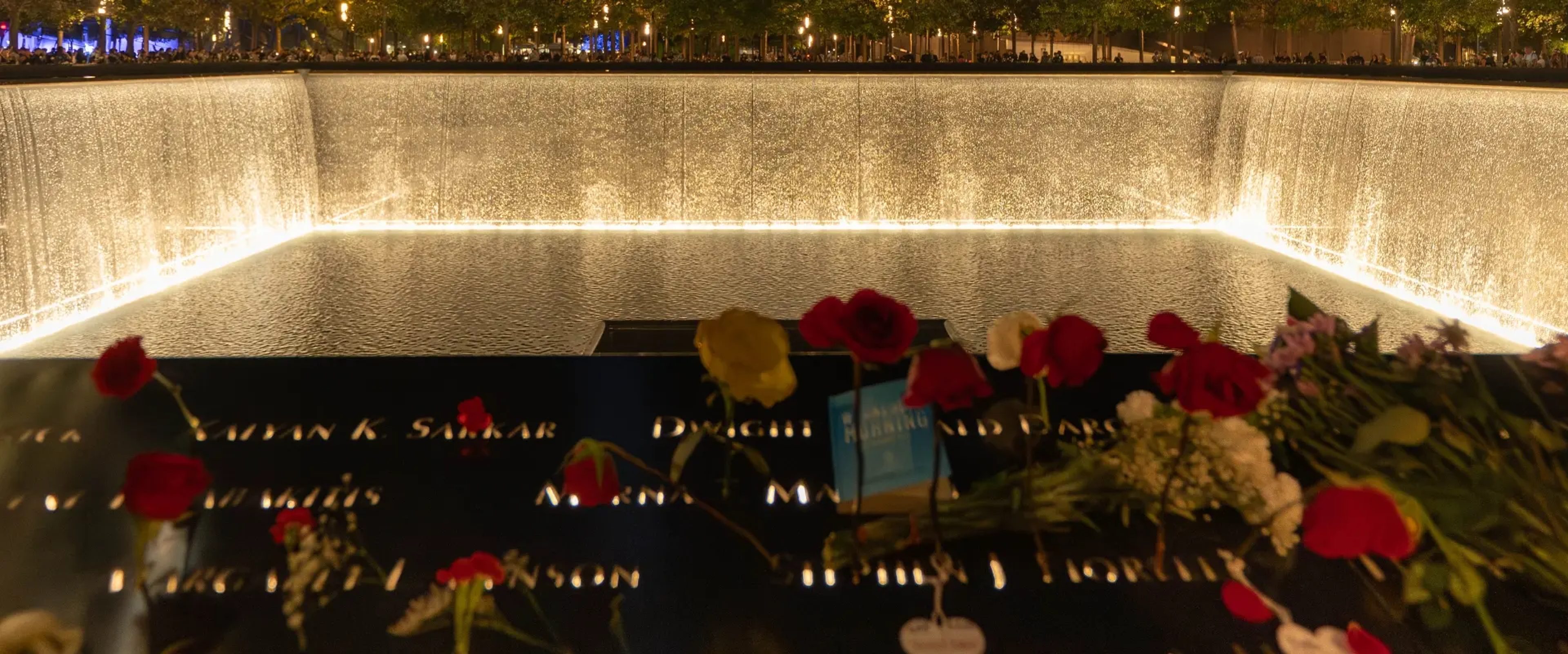 9/11 Memorial pool lit at night and decorated with roses