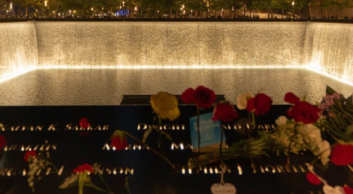 9/11 Memorial pool lit at night and decorated with roses