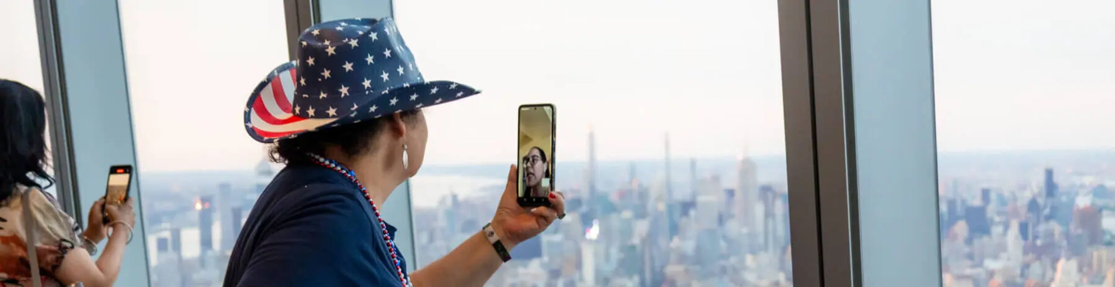 Person with hat in USA colors taking a photo of New York