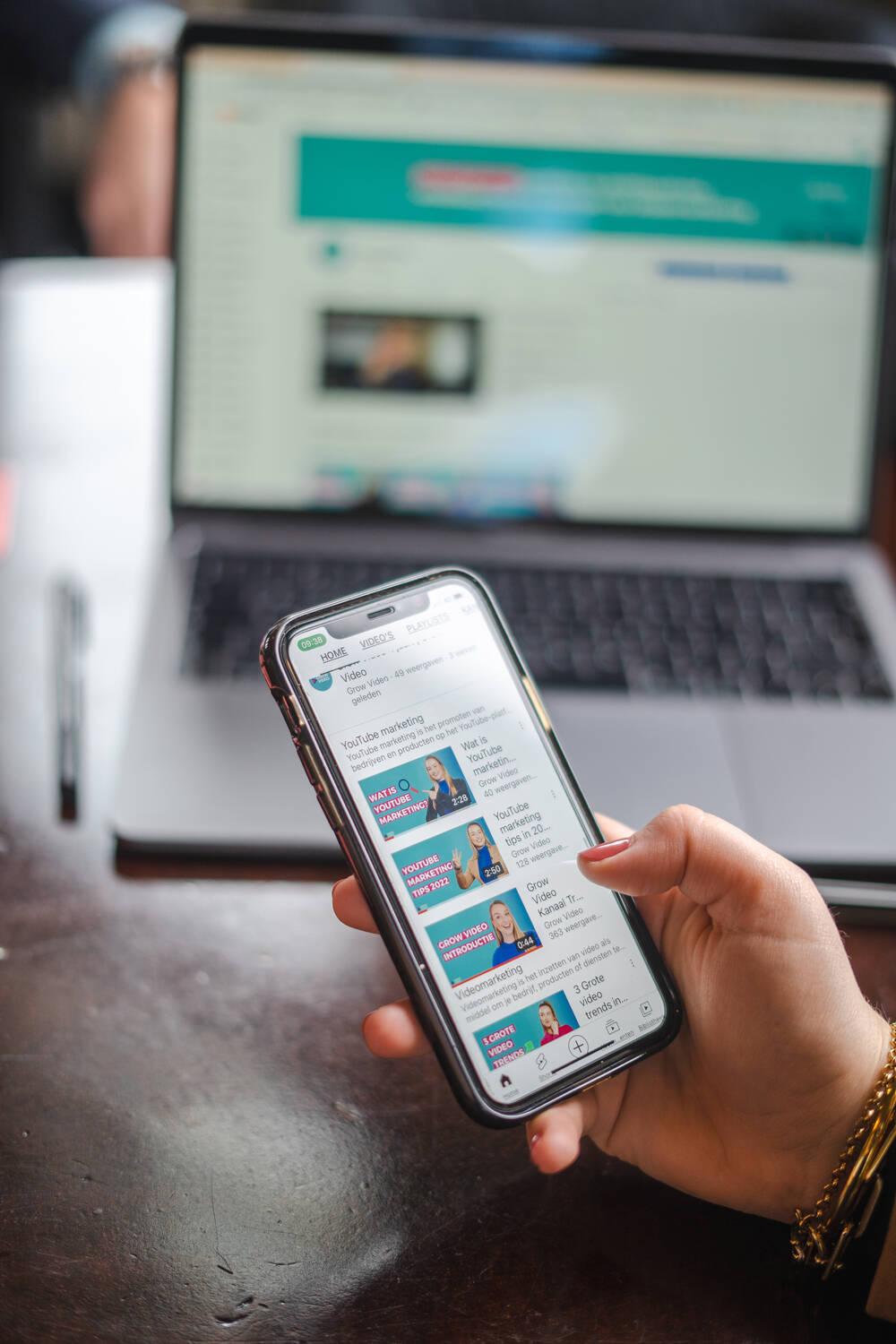 Smartphone met YouTube-video's in een hand, voor een laptop