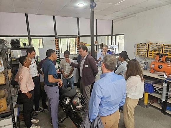 Werkstattbesuch in Pune: Die Delegation steht um ein auf Wasserstoff umgerüstetes Motorrad, ein Ingenieur erläutert die Technik