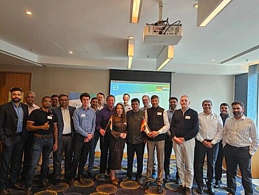 Deutsche und indische Teilnehmende im Konferenzraum in Pune, in der Mitte zwei Personen mit kleinen Landesflaggen