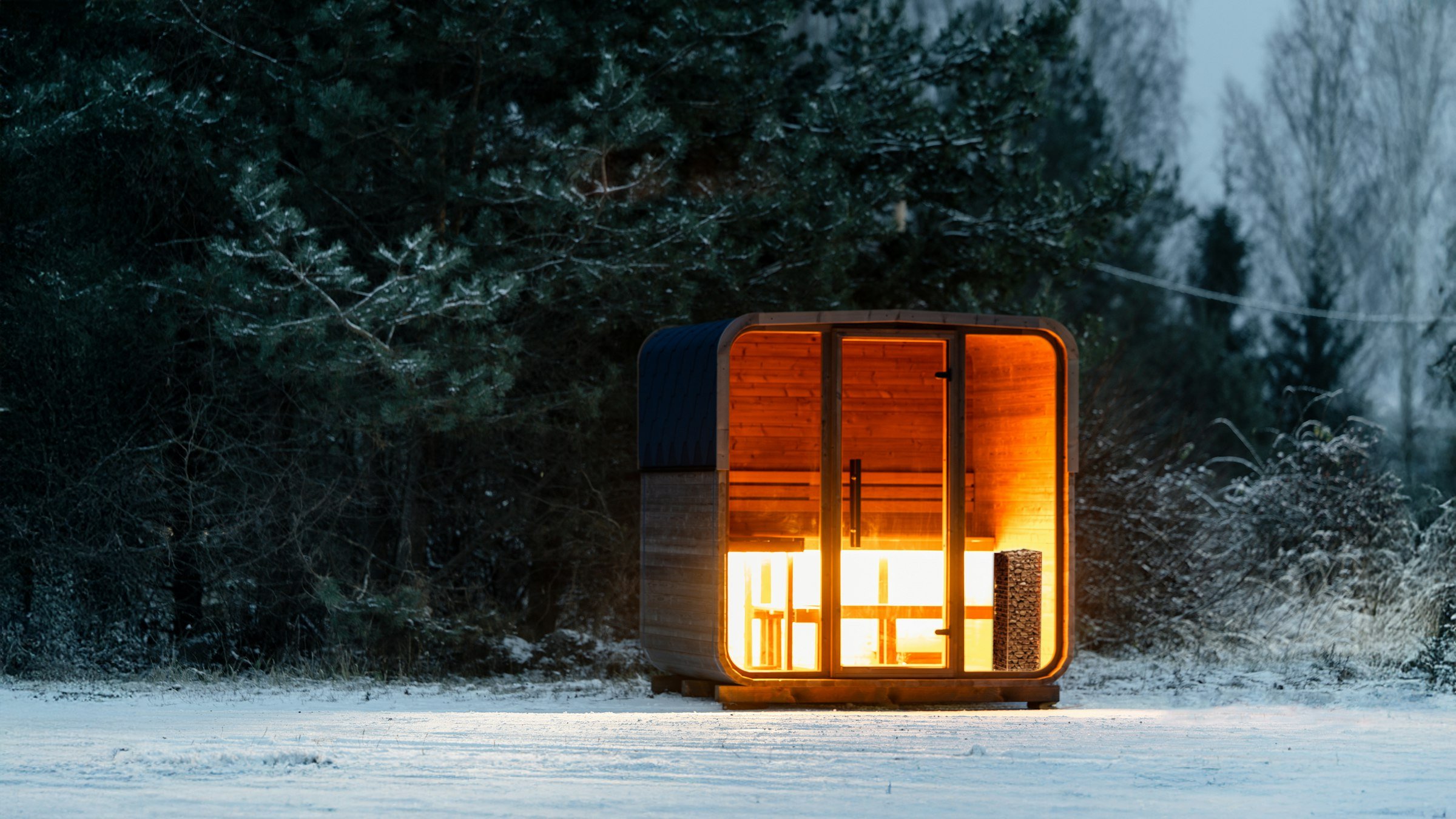 Cabine sauna illuminée dans une forêt enneigée au crépuscule