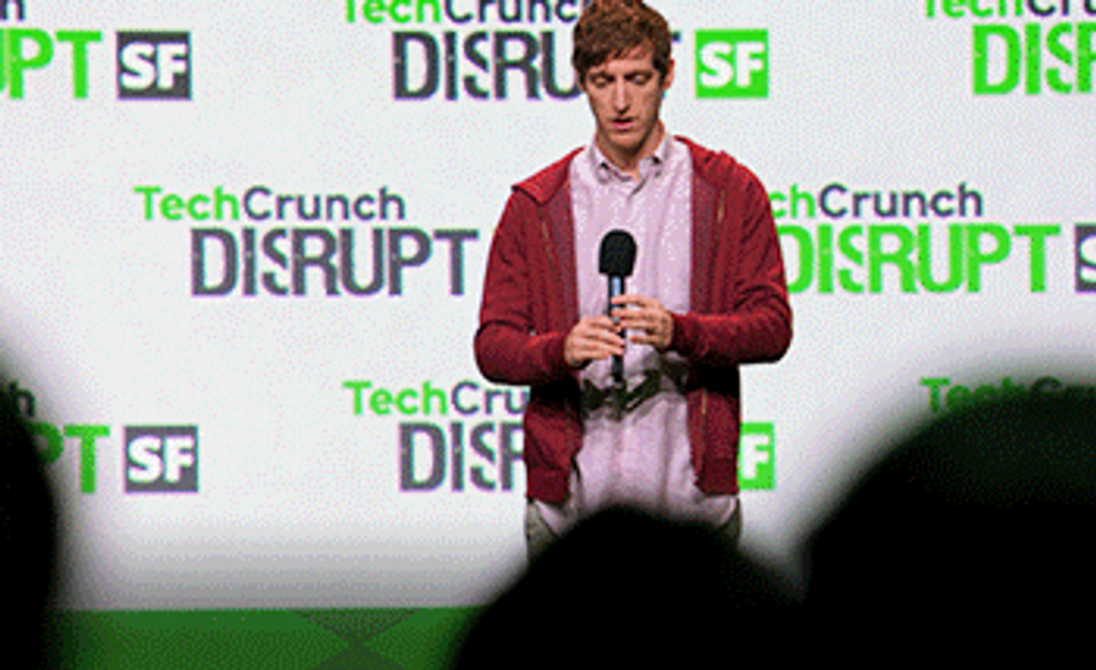 A man holding a microphone onstage in front of a backdrop repeating "TechCrunch Disrupt SF".