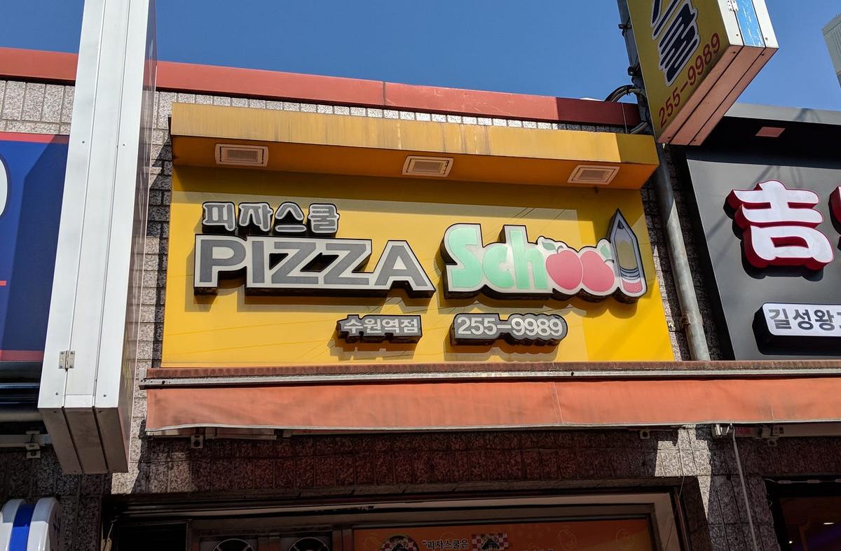 Yellow storefront sign reading "PIZZA School" in Korean and English, with a giant pencil and phone number 255-9989.