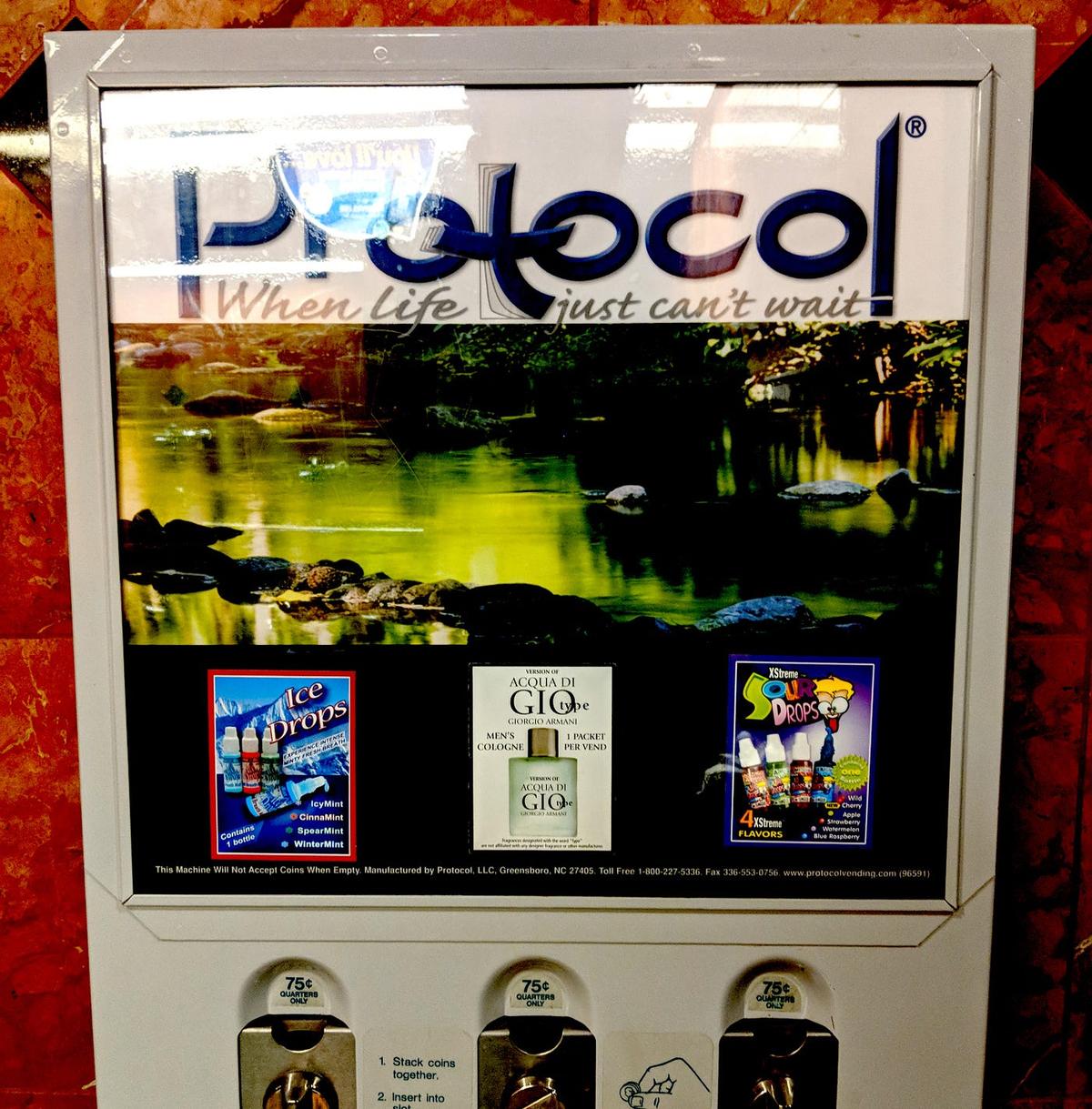 Restroom vending machine branded "Protocol — When life just can't wait," selling Ice Drops, Acqua Di Gio cologne and XStreme Sour Drops at 75\u00a2.