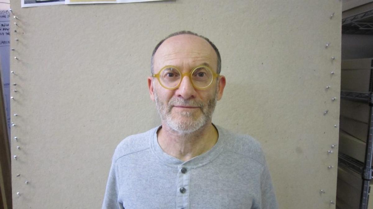 Danny Altman, in round yellow glasses and a gray henley, in front of a pinboard.