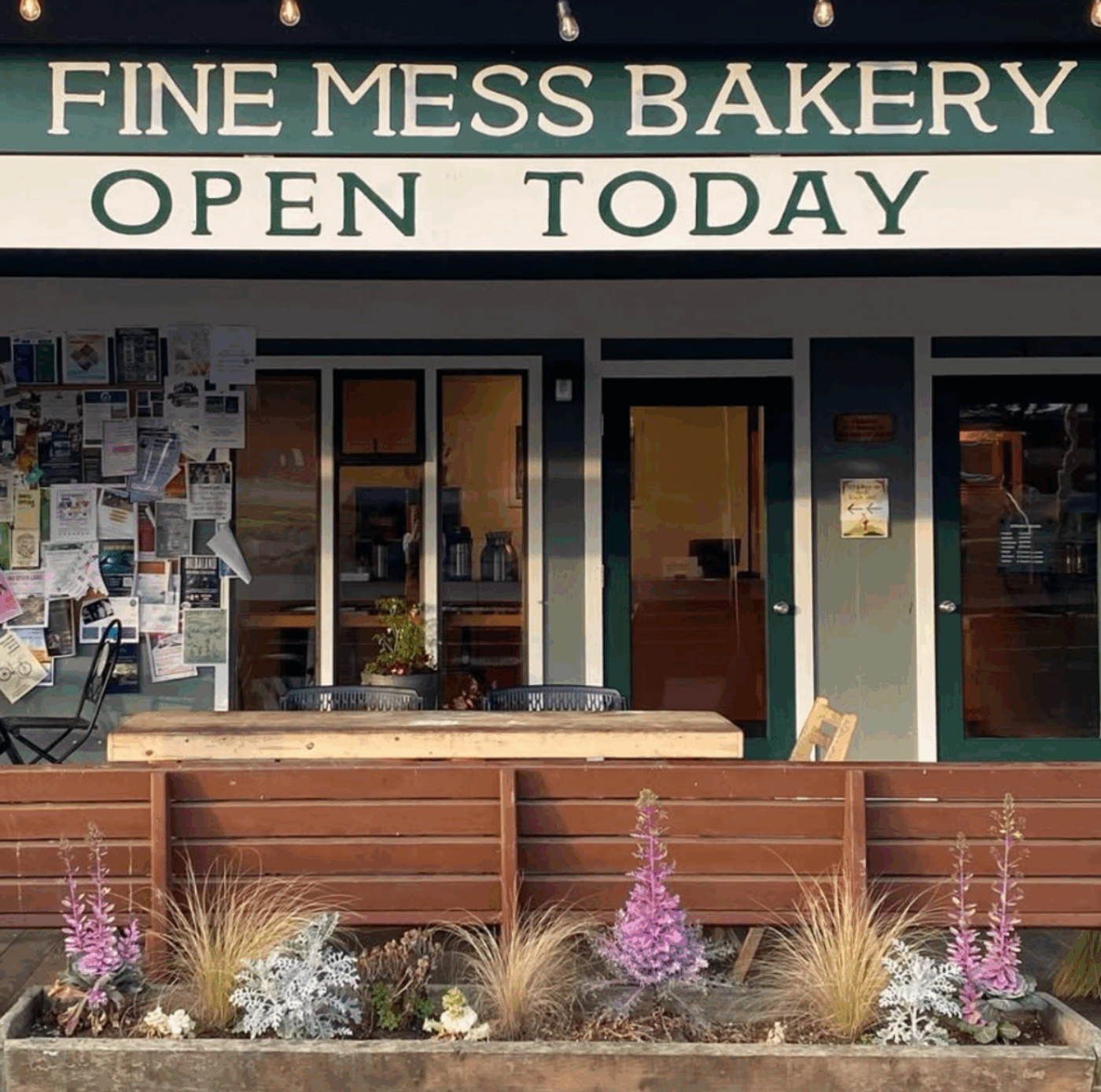 The bakery shopfront, FINE MESS BAKERY painted across the awning above an OPEN TODAY board, planters of grasses and lupins along the front