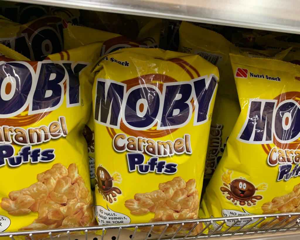 Yellow bags of "Moby Caramel Puffs" on a supermarket shelf.
