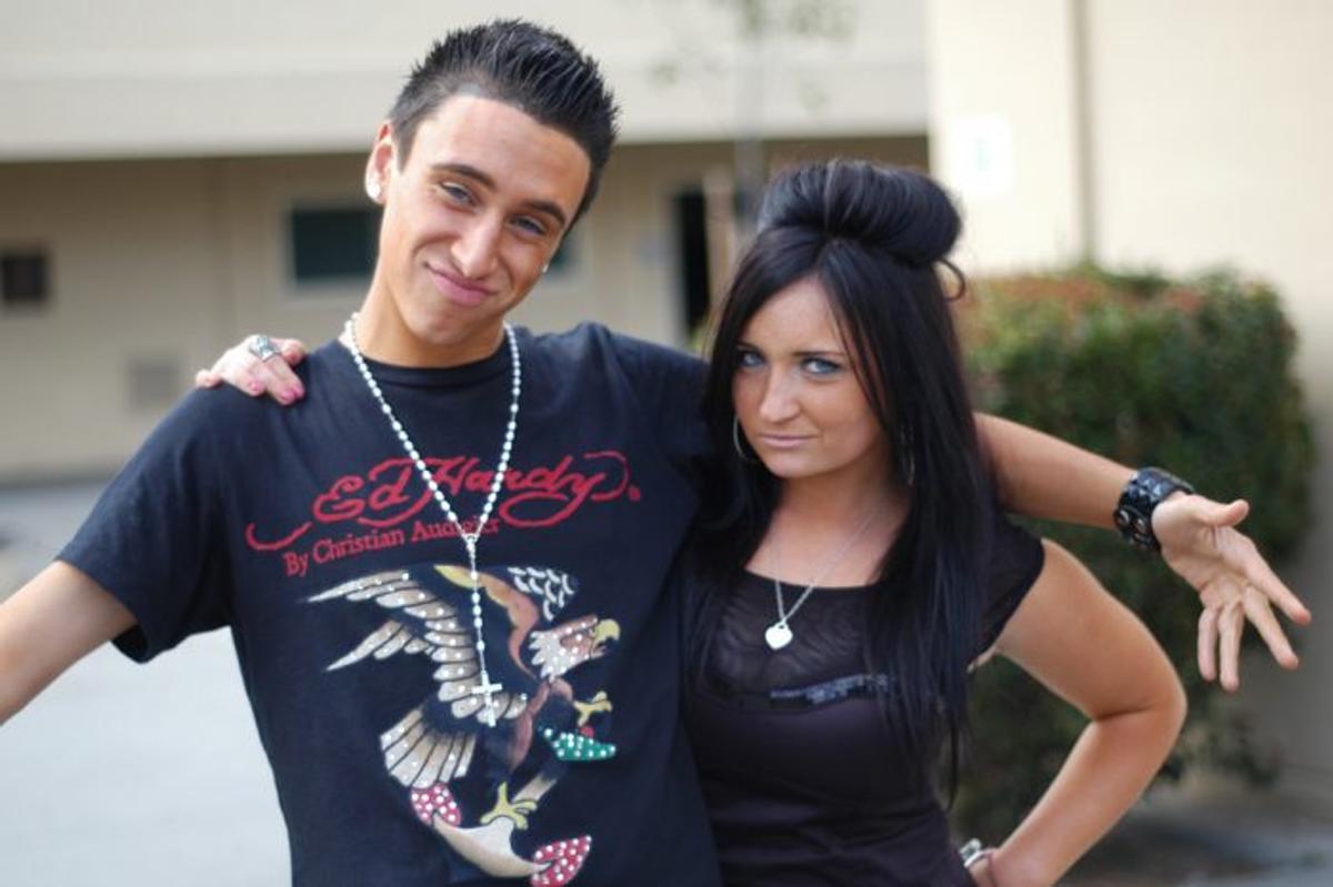 A young man in an Ed Hardy T-shirt poses with a woman with teased black hair.